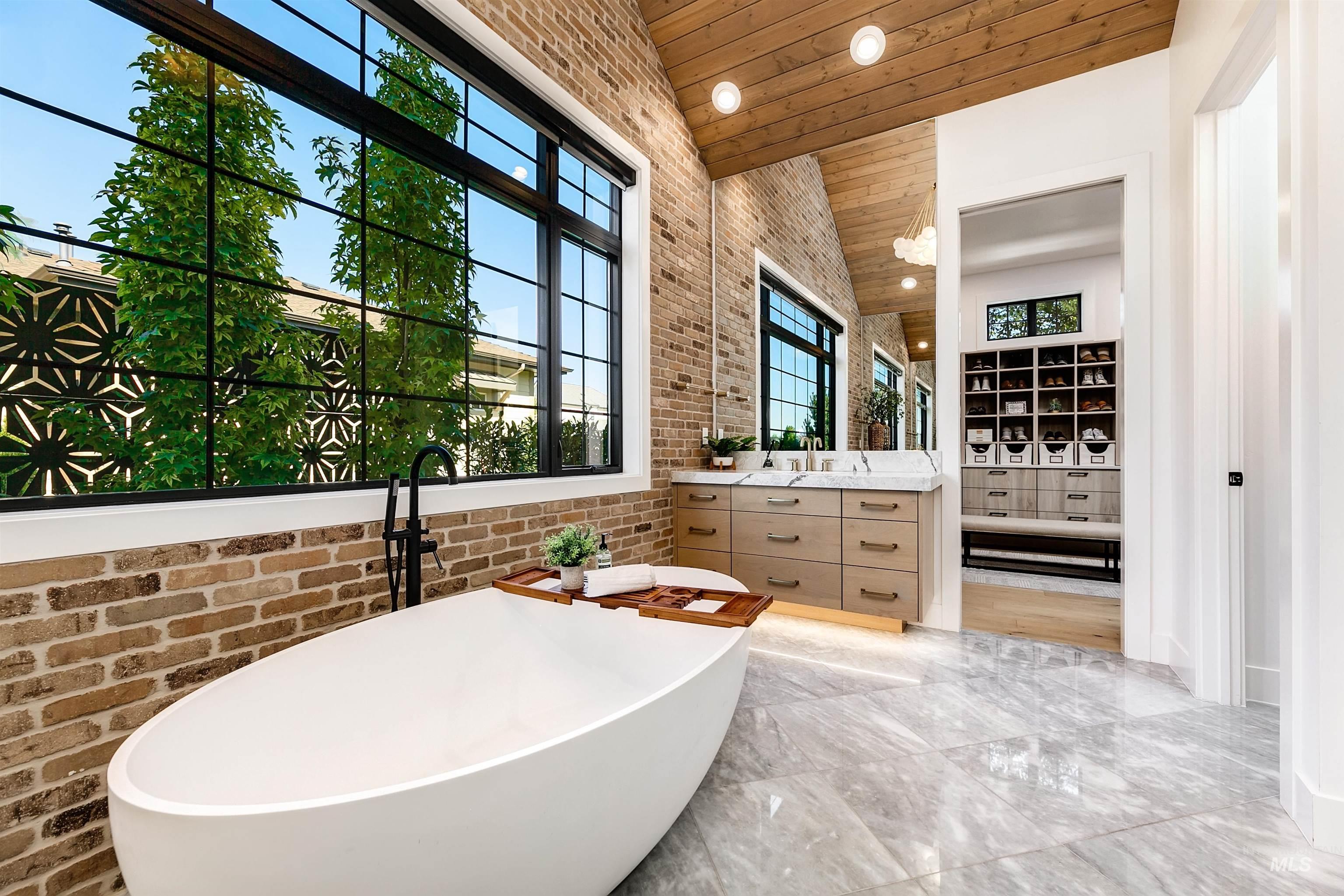 Full bath featuring brick wall, a freestanding bath, vanity, wood ceiling, and light marble finish floors