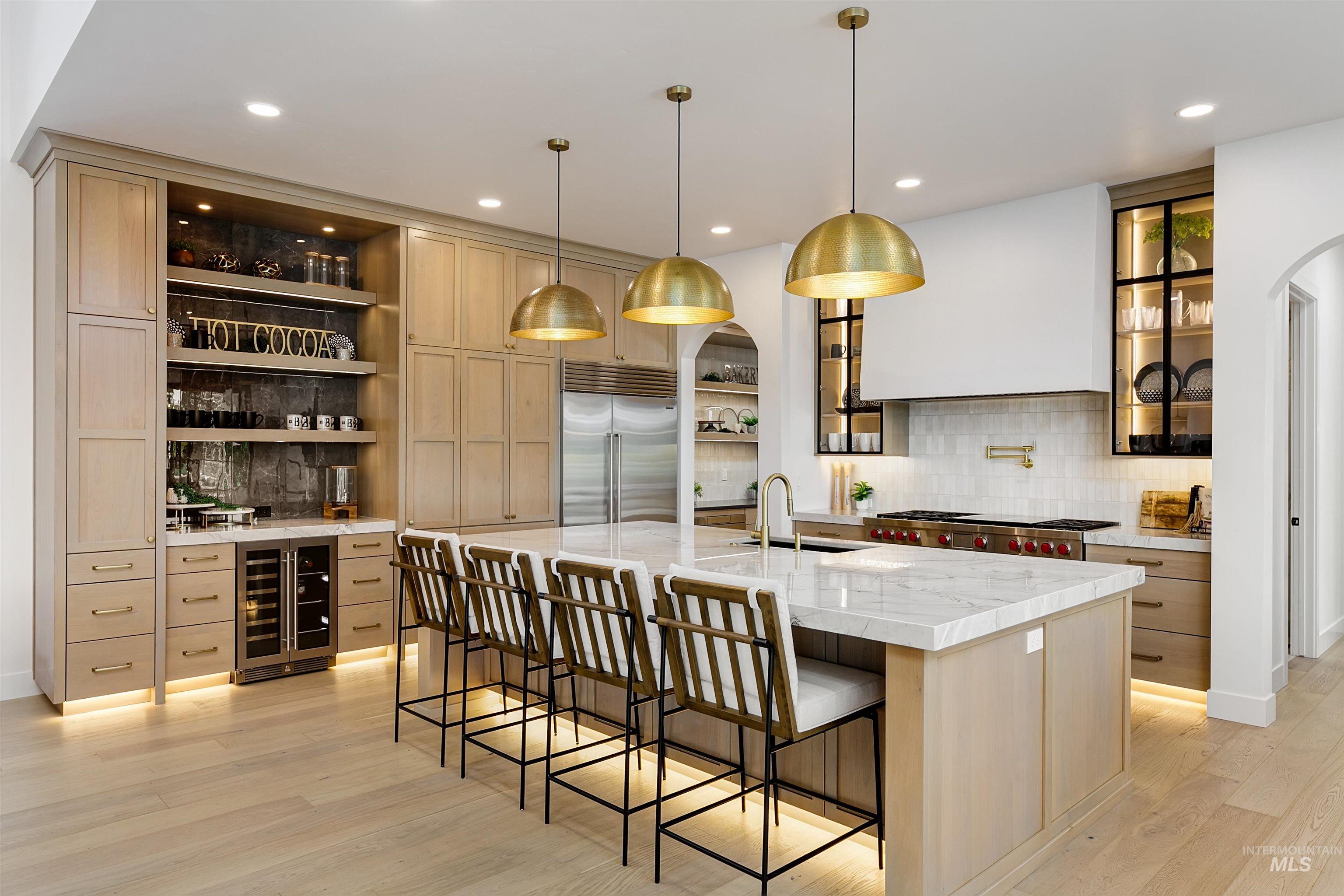 Kitchen with light stone countertops, decorative light fixtures, a breakfast bar, light brown cabinets, and wine cooler