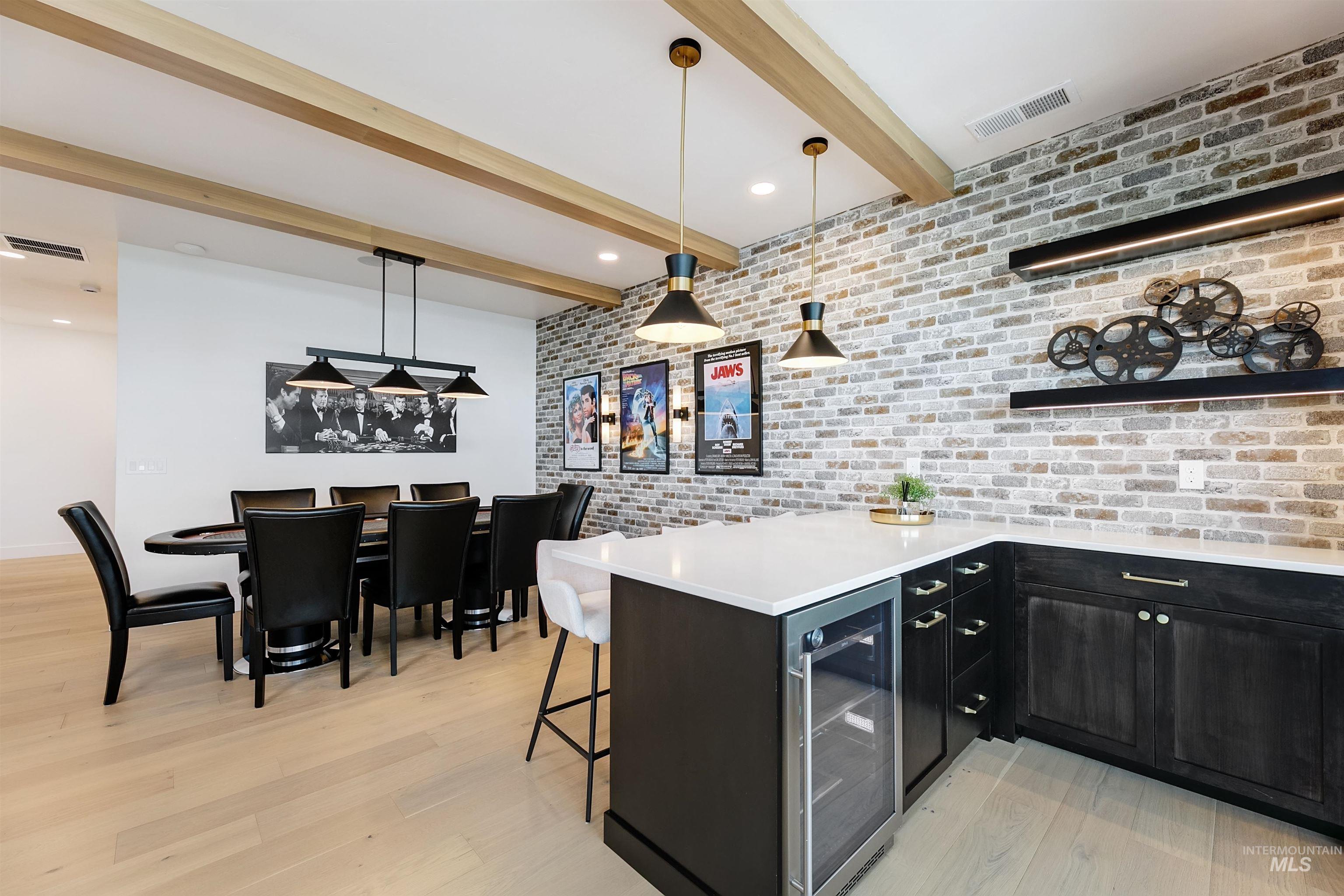 Kitchen with brick wall, a peninsula, dark cabinets, beamed ceiling, and decorative light fixtures