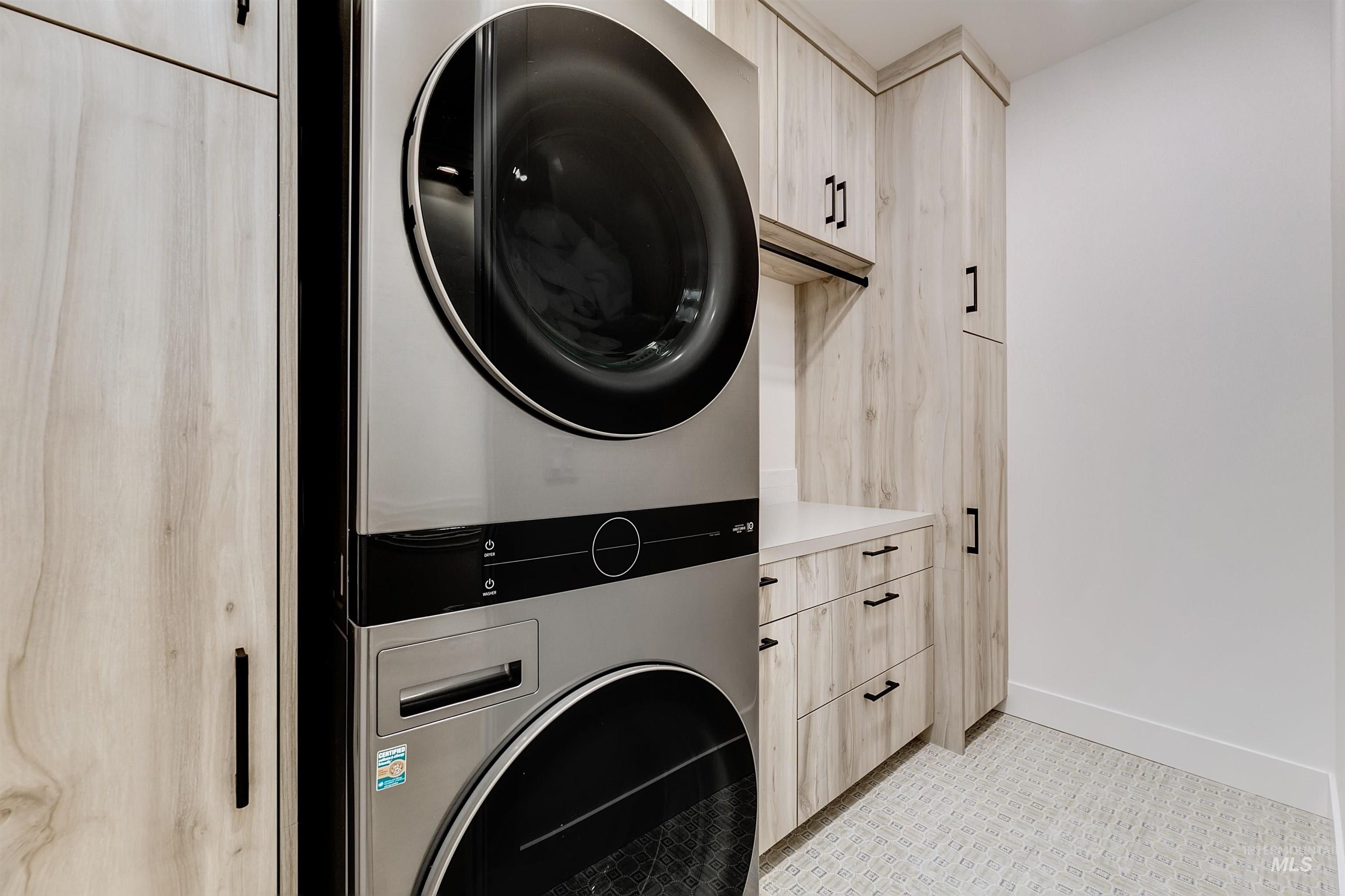 Washroom with cabinet space, stacked washer / dryer, and light tile patterned floors