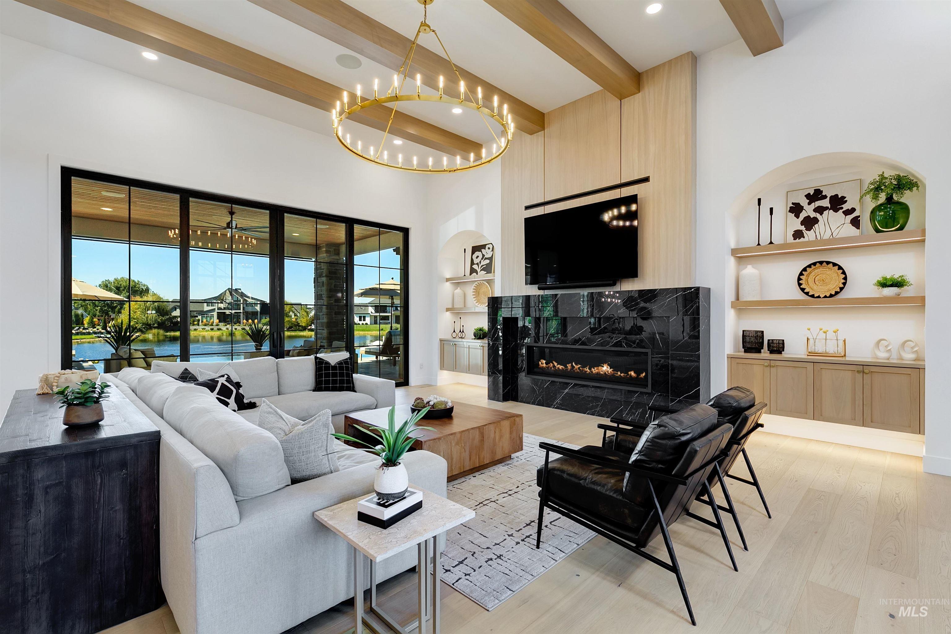 Living area featuring beamed ceiling, a high end fireplace, light wood finished floors, built in shelves, and a chandelier