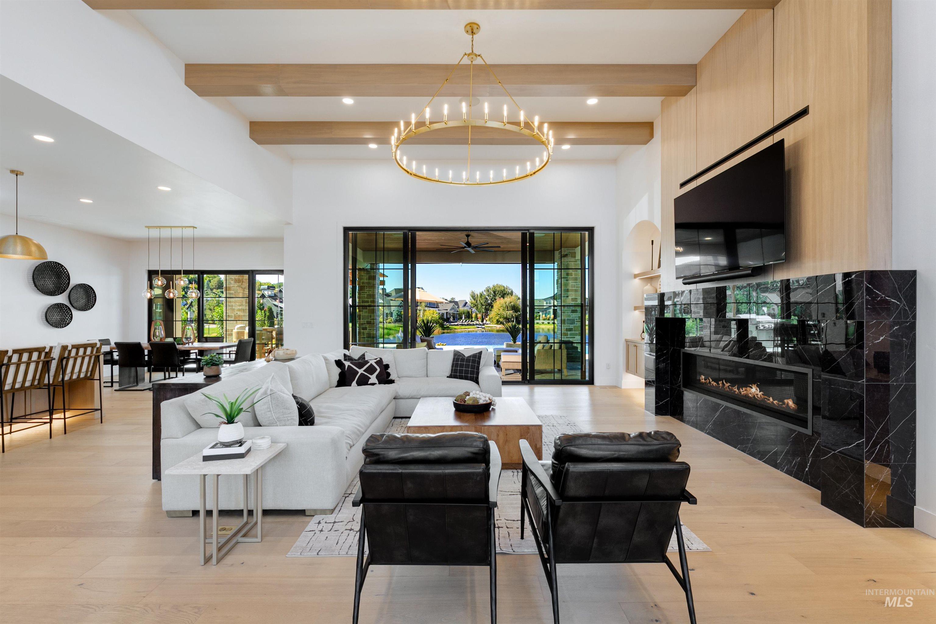Living area featuring beamed ceiling, a chandelier, light wood finished floors, a glass covered fireplace, and recessed lighting