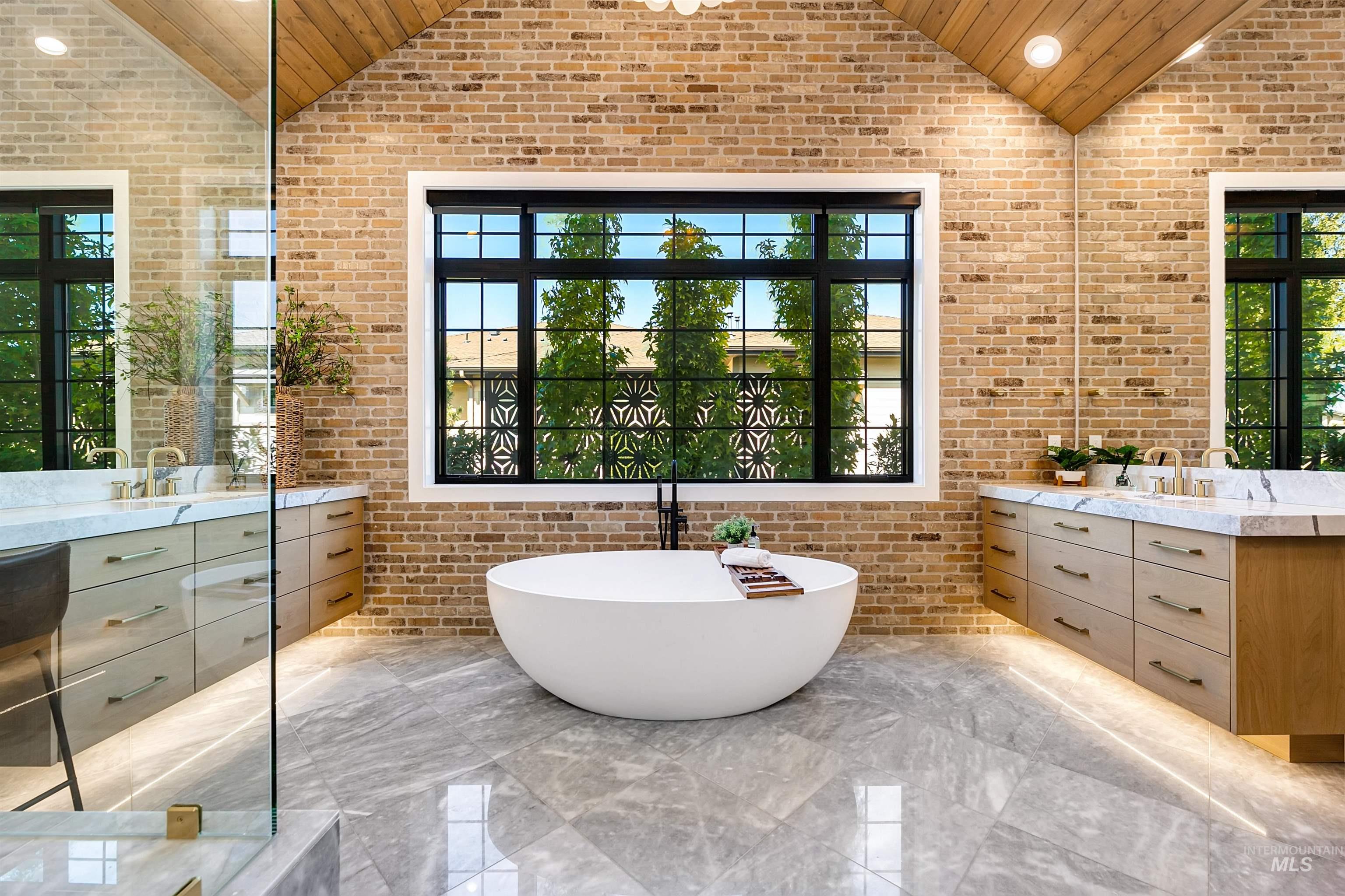 Full bathroom with brick wall, a soaking tub, vaulted ceiling, two vanities, and plenty of natural light