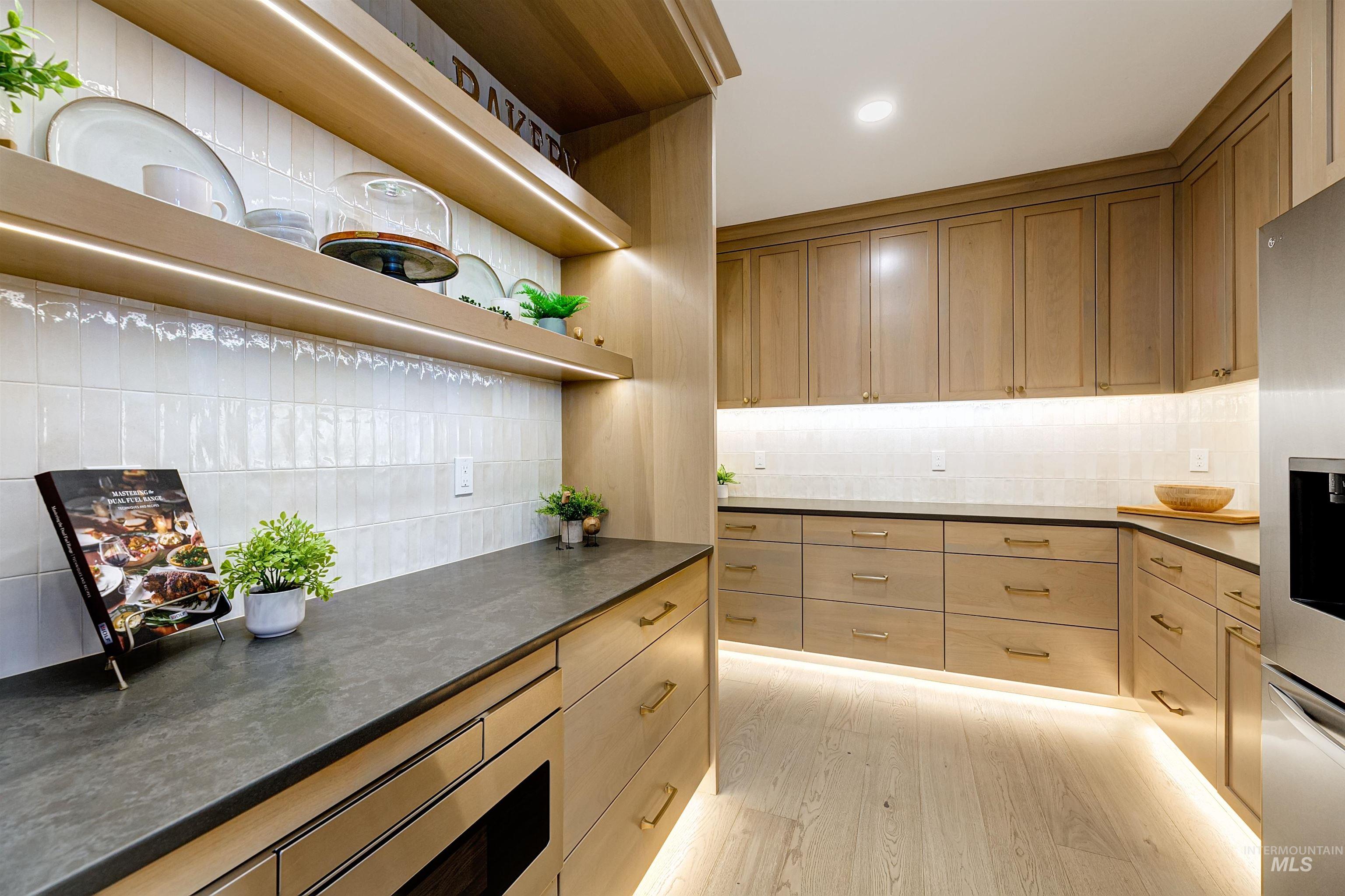 Kitchen with light wood-style floors, decorative backsplash, dark stone countertops, stainless steel refrigerator with ice dispenser, and light brown cabinetry