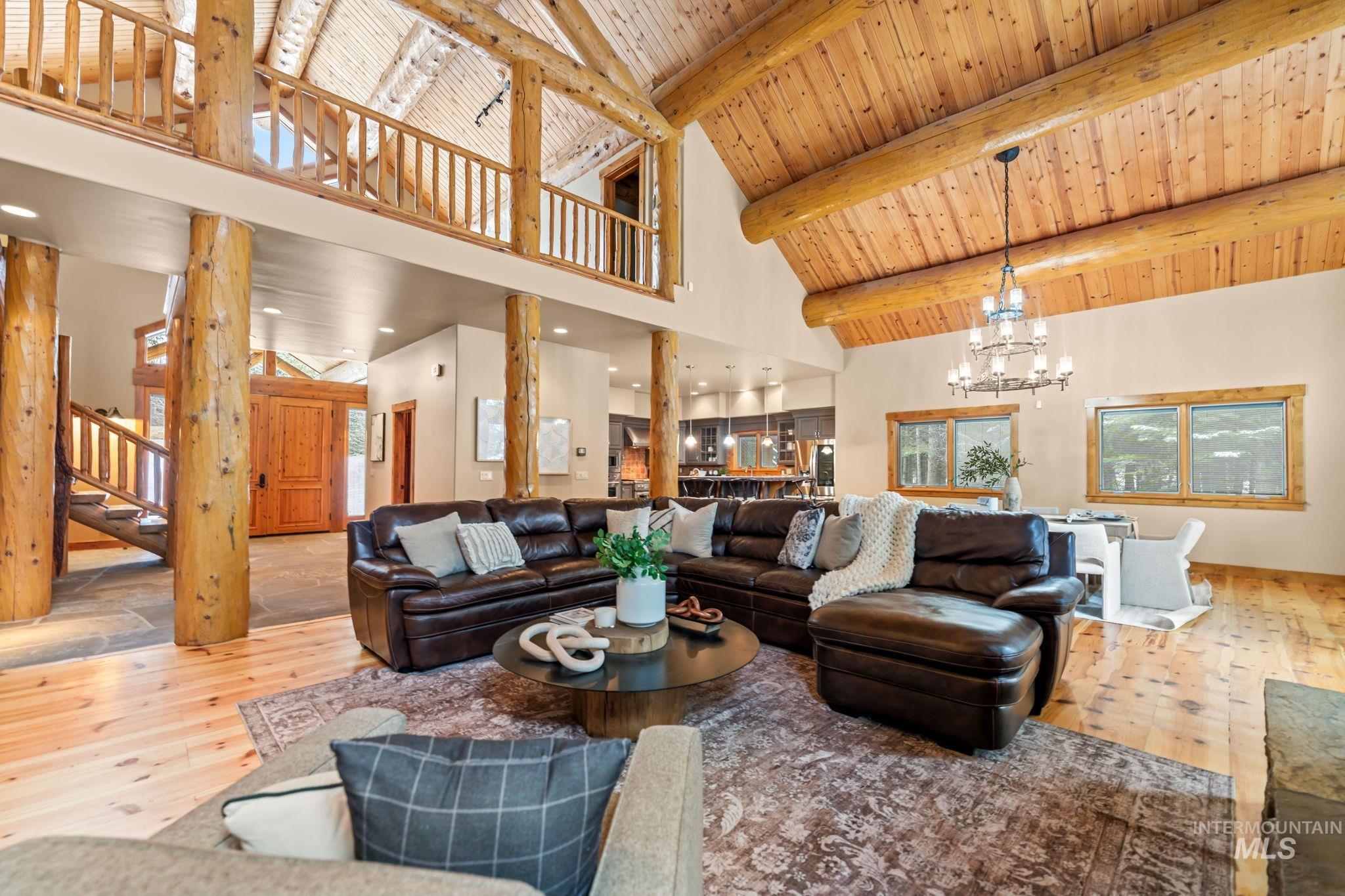 Living room with a chandelier, high vaulted ceiling, light wood-type flooring, stairs, and a wooden ceiling with exposed beams