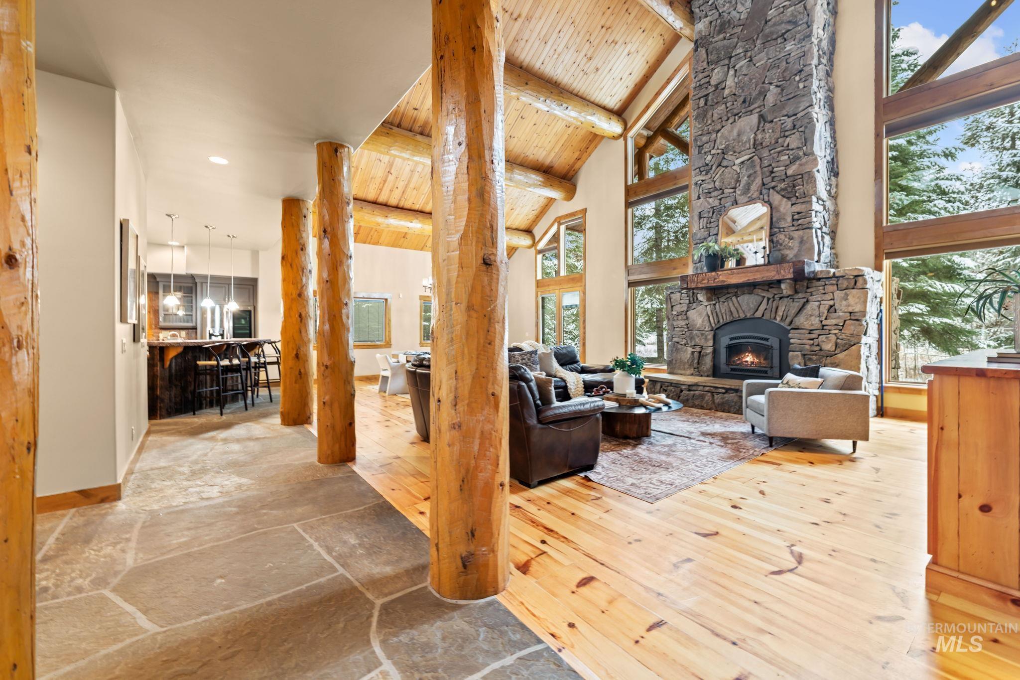 Living room with a wooden ceiling with exposed beams, stone tile floors, high vaulted ceiling, and a stone fireplace