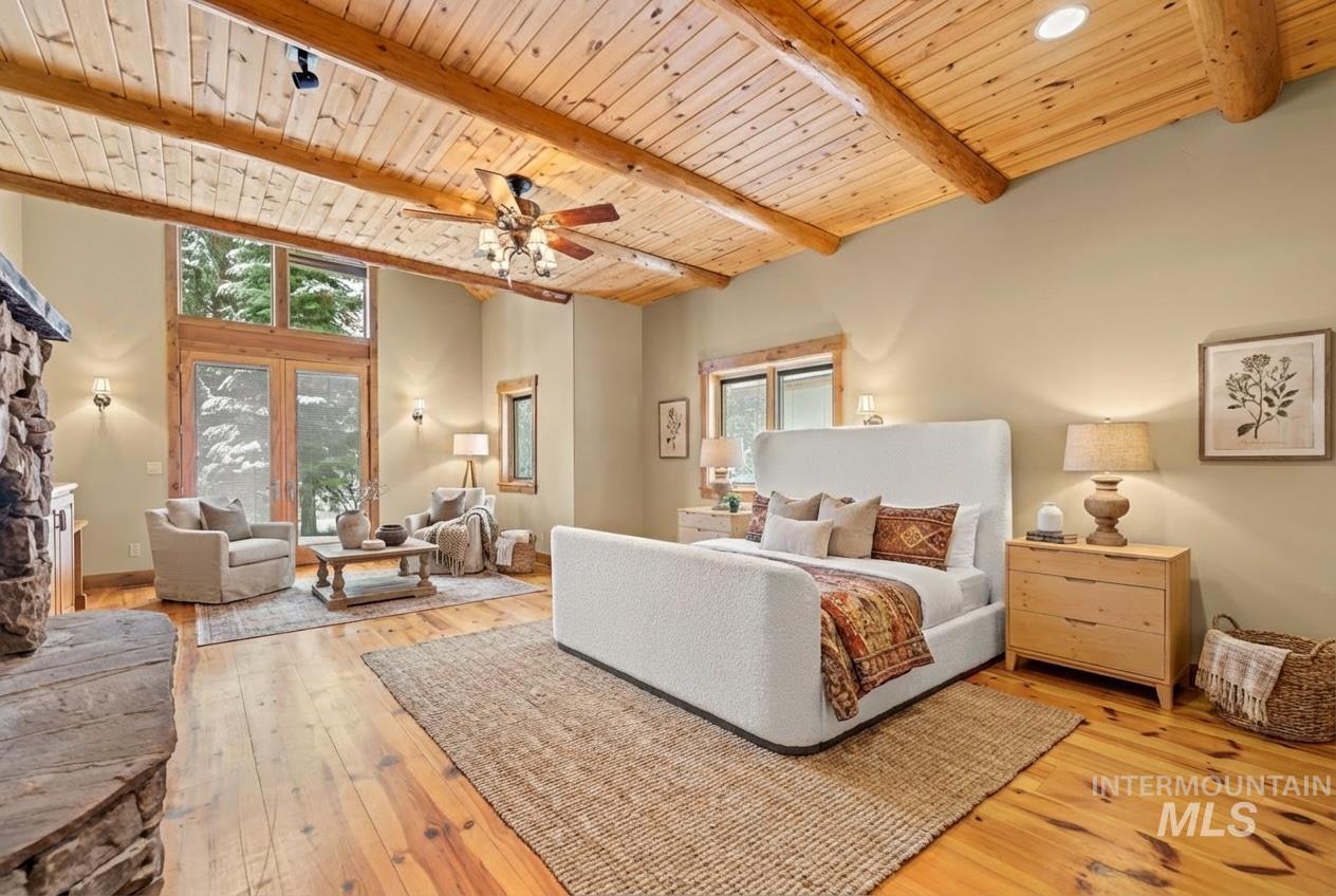 Bedroom with a wood ceiling with exposed beams, light wood-type flooring, a fireplace, ceiling fan, and a high ceiling