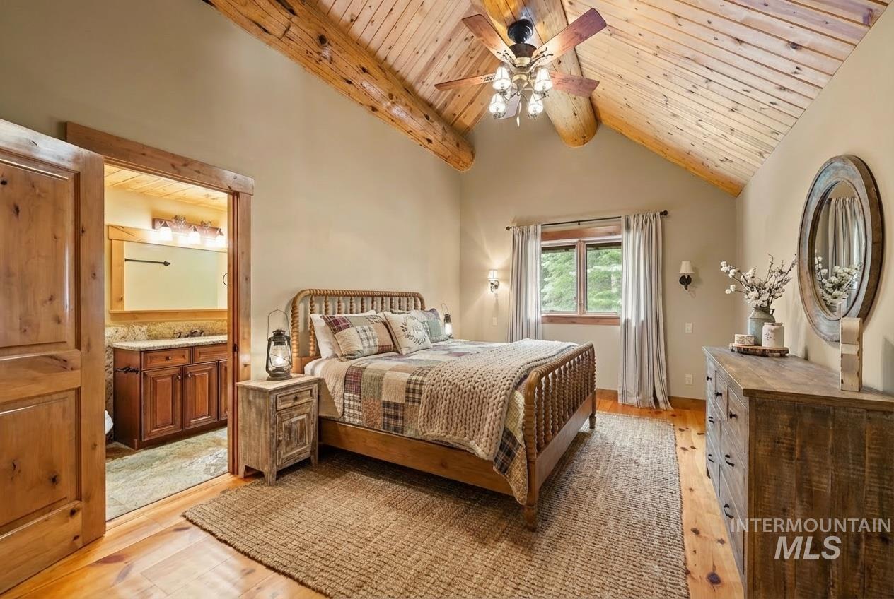 Bedroom with a wood ceiling with exposed beams, light wood finished floors, high vaulted ceiling, ensuite bath, and a ceiling fan