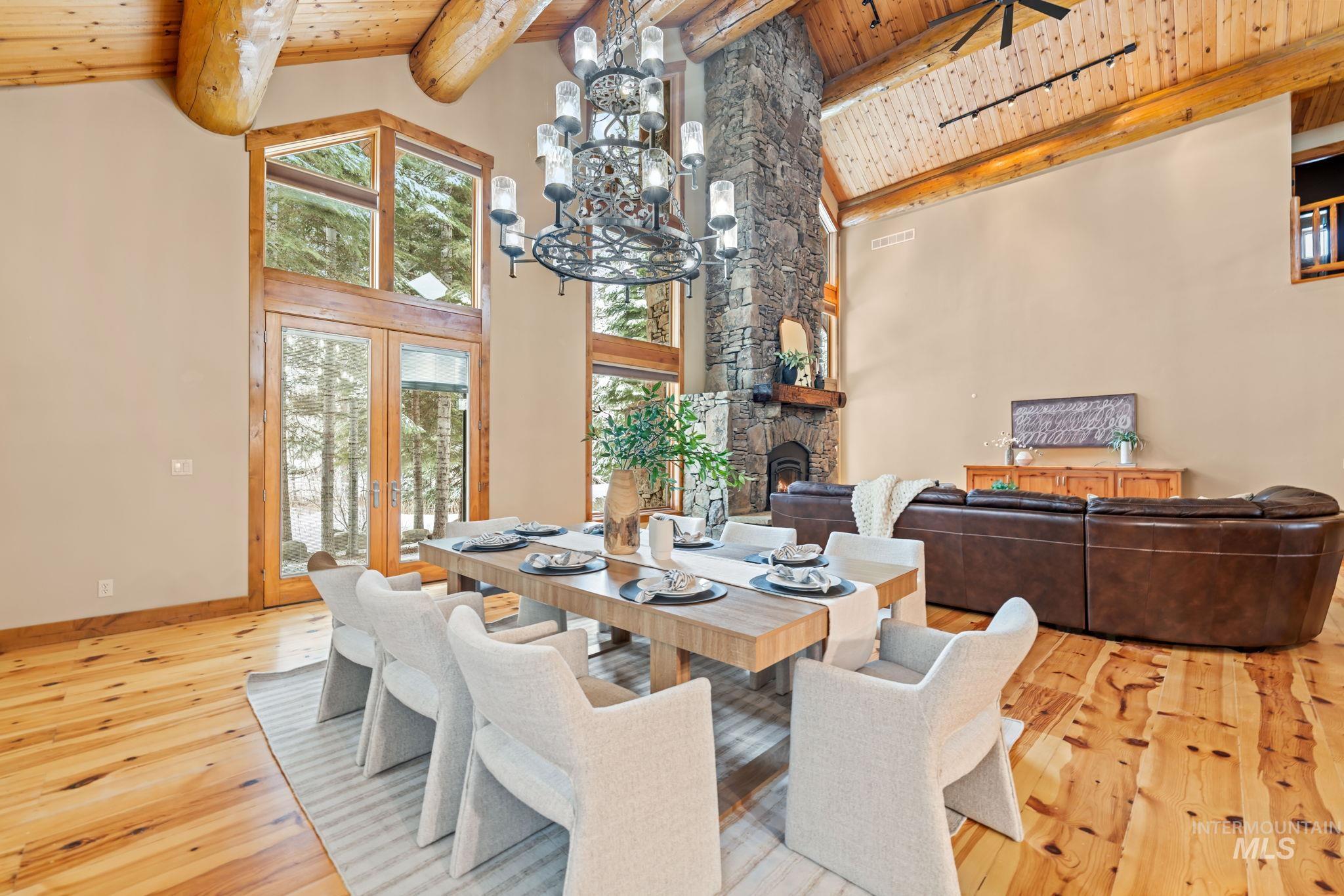 Dining area featuring a chandelier, light wood-style floors, a fireplace, french doors, and a wooden ceiling with exposed beams