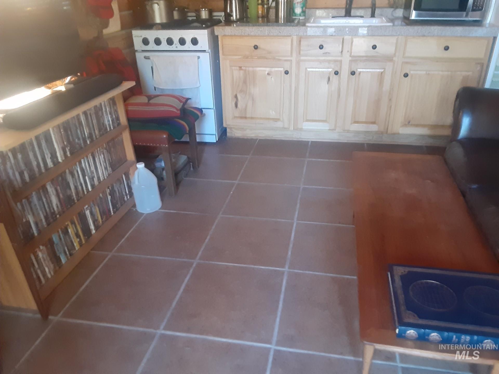 Kitchen with dark tile patterned floors, white stove, stainless steel microwave, electric cooktop, and light countertops