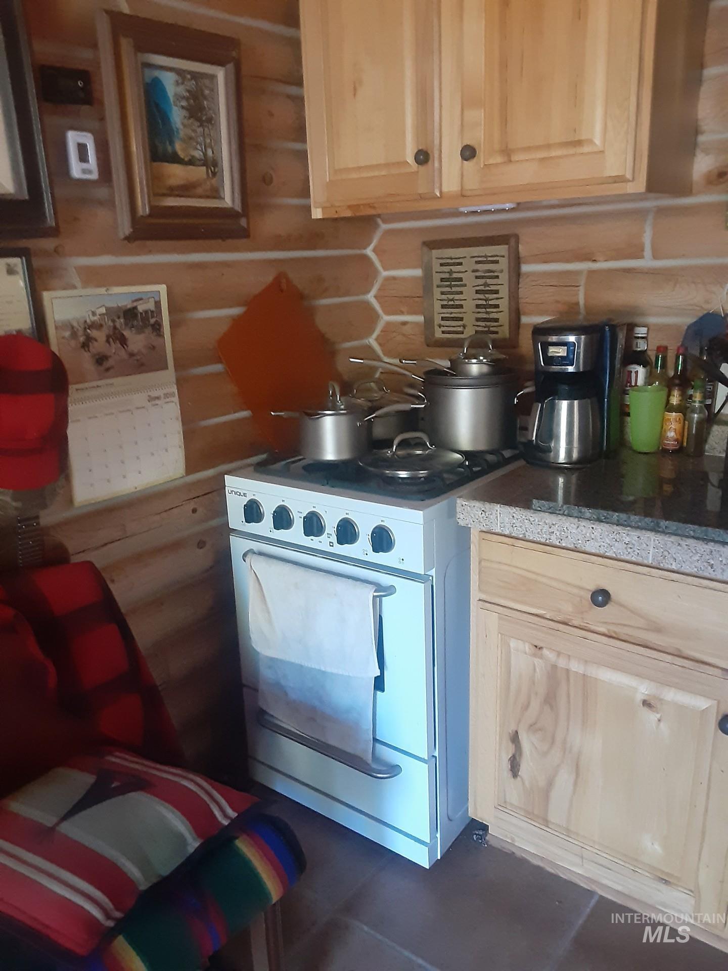 Kitchen with light brown cabinetry, white stove, rustic walls, and dark tile patterned flooring