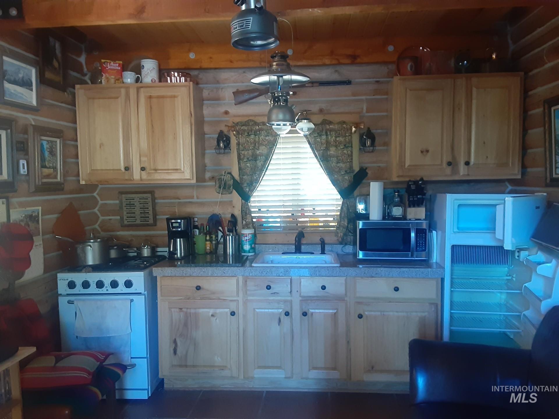 Kitchen with white range, rustic walls, stainless steel microwave, fridge, and light brown cabinetry
