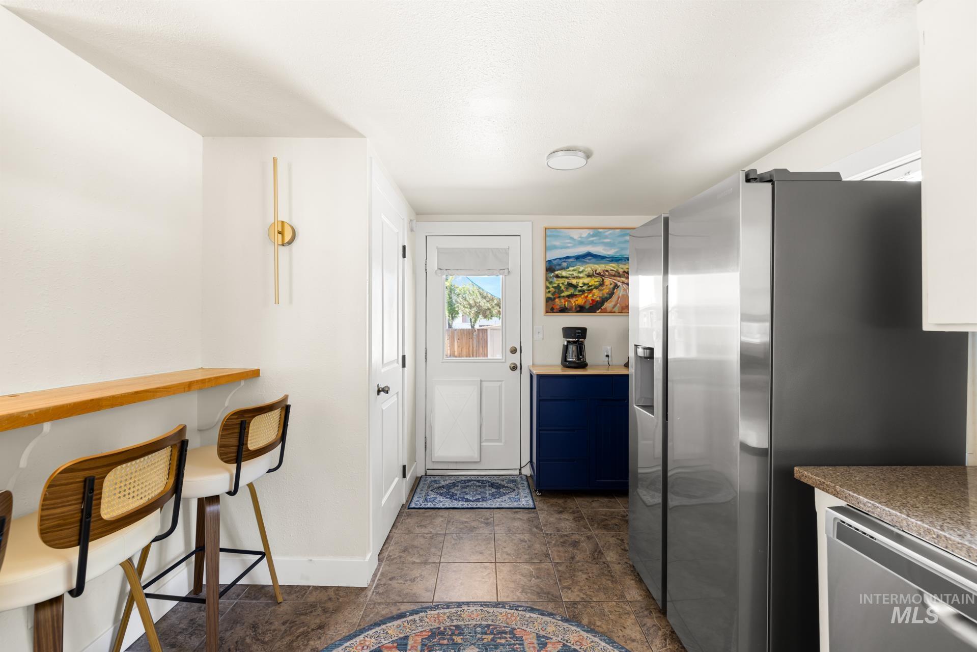 Compact kitchen featuring a stainless steel refrigerator, tile flooring, and a wood-finish bar-height counter