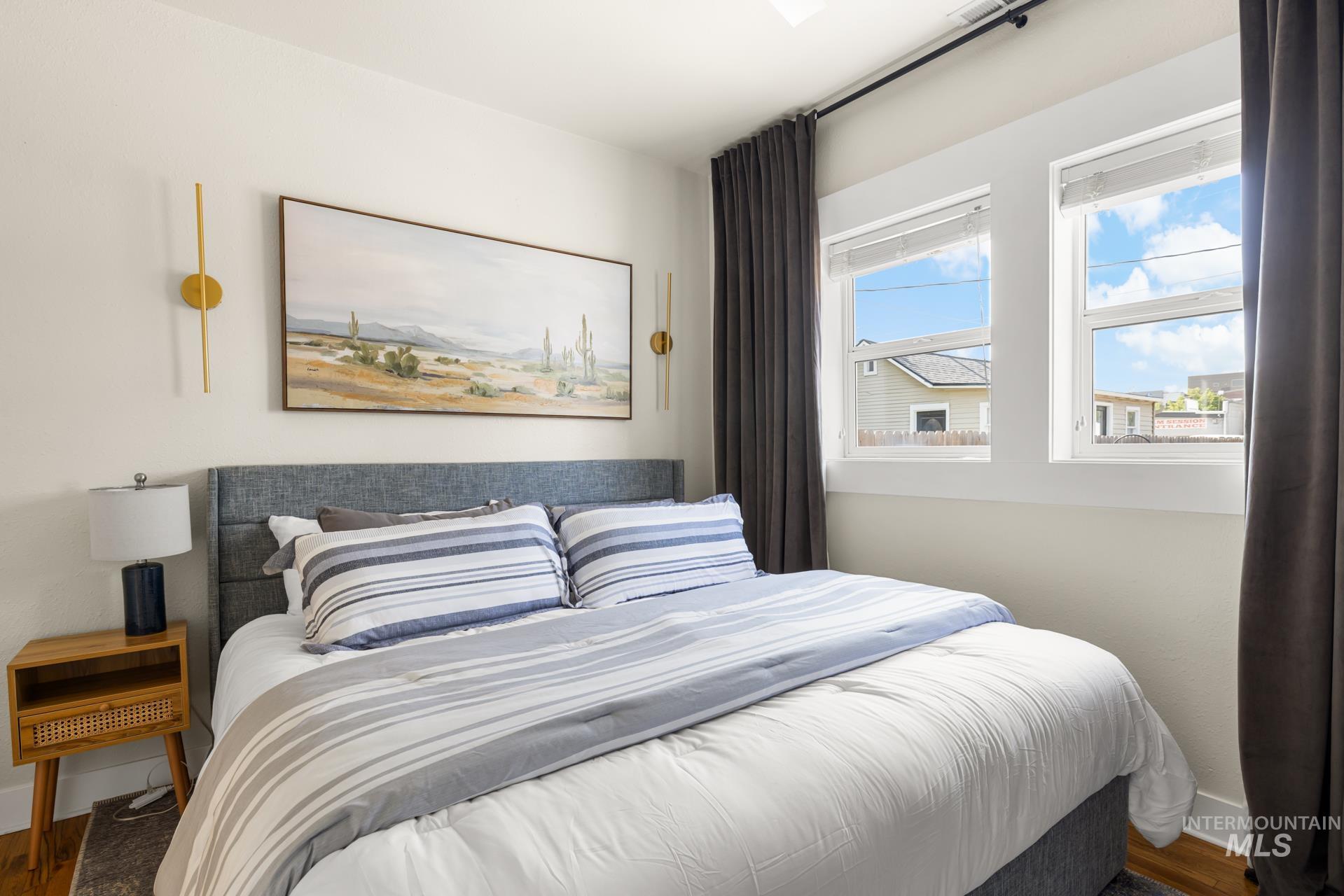 Bedroom featuring twin windows with white trim, a fabric upholstered headboard, and wood-finish flooring