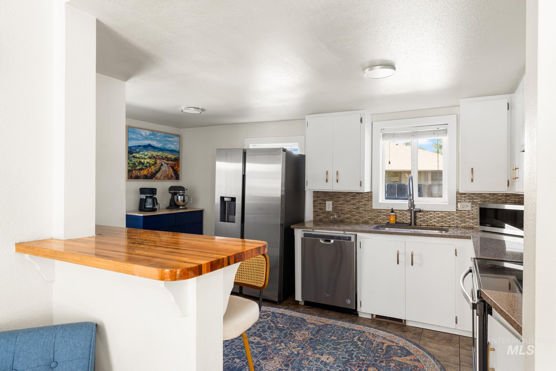 Kitchen featuring a wood-finish peninsula, white cabinetry, stainless steel appliances, and a mosaic tile backsplash