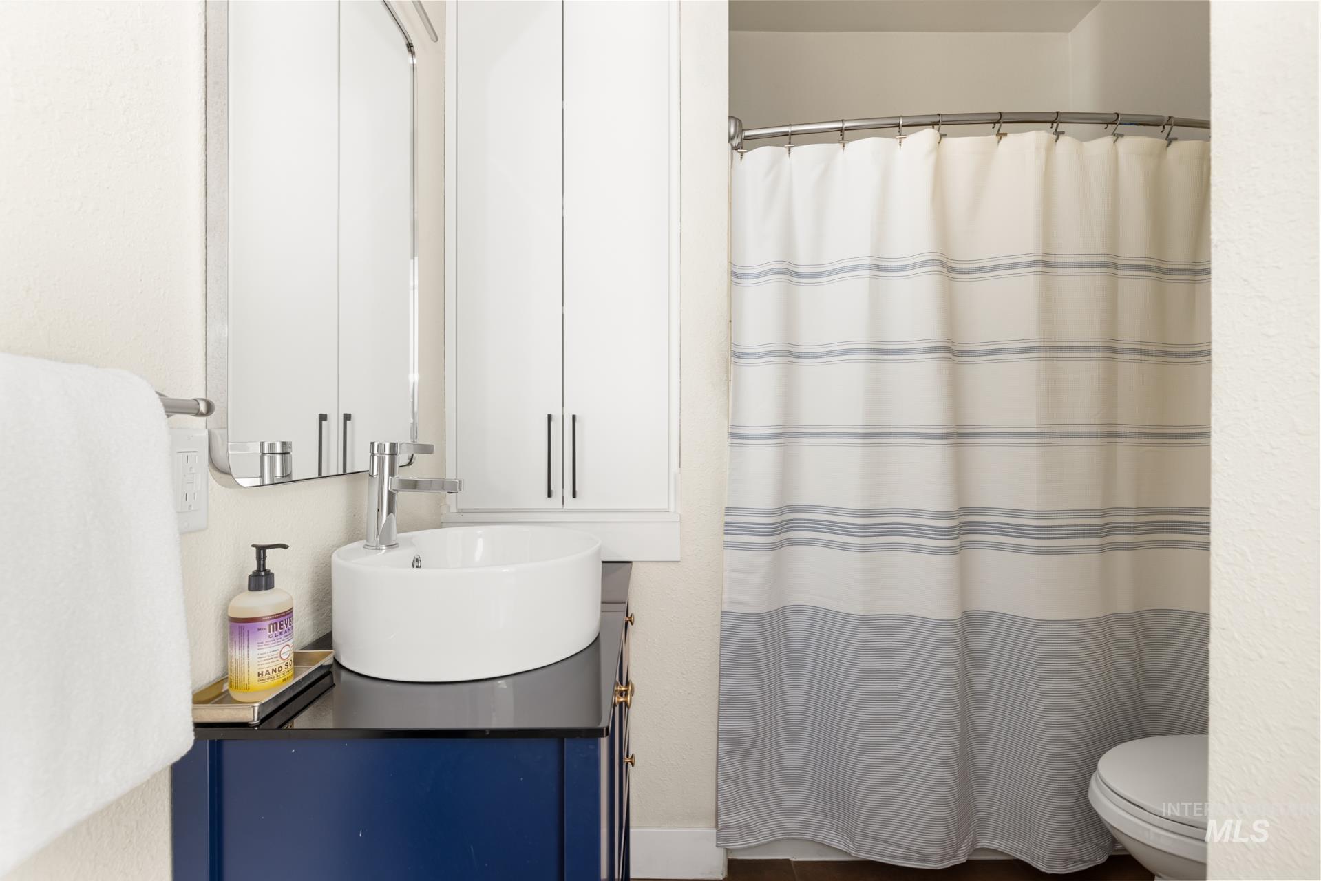Modern bathroom featuring a circular vessel sink, chrome faucet, and a dark blue vanity with a black countertop