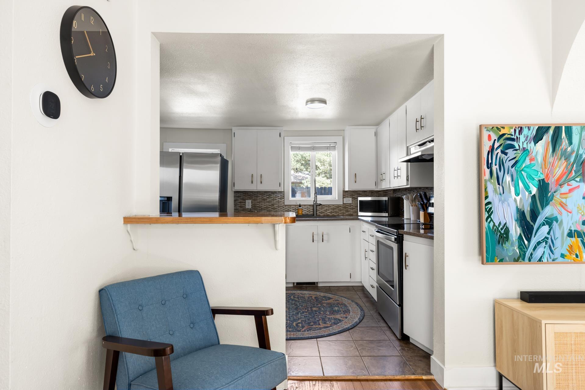 Kitchen featuring white cabinetry, stainless steel appliances, dark countertops, and a tiled backsplash