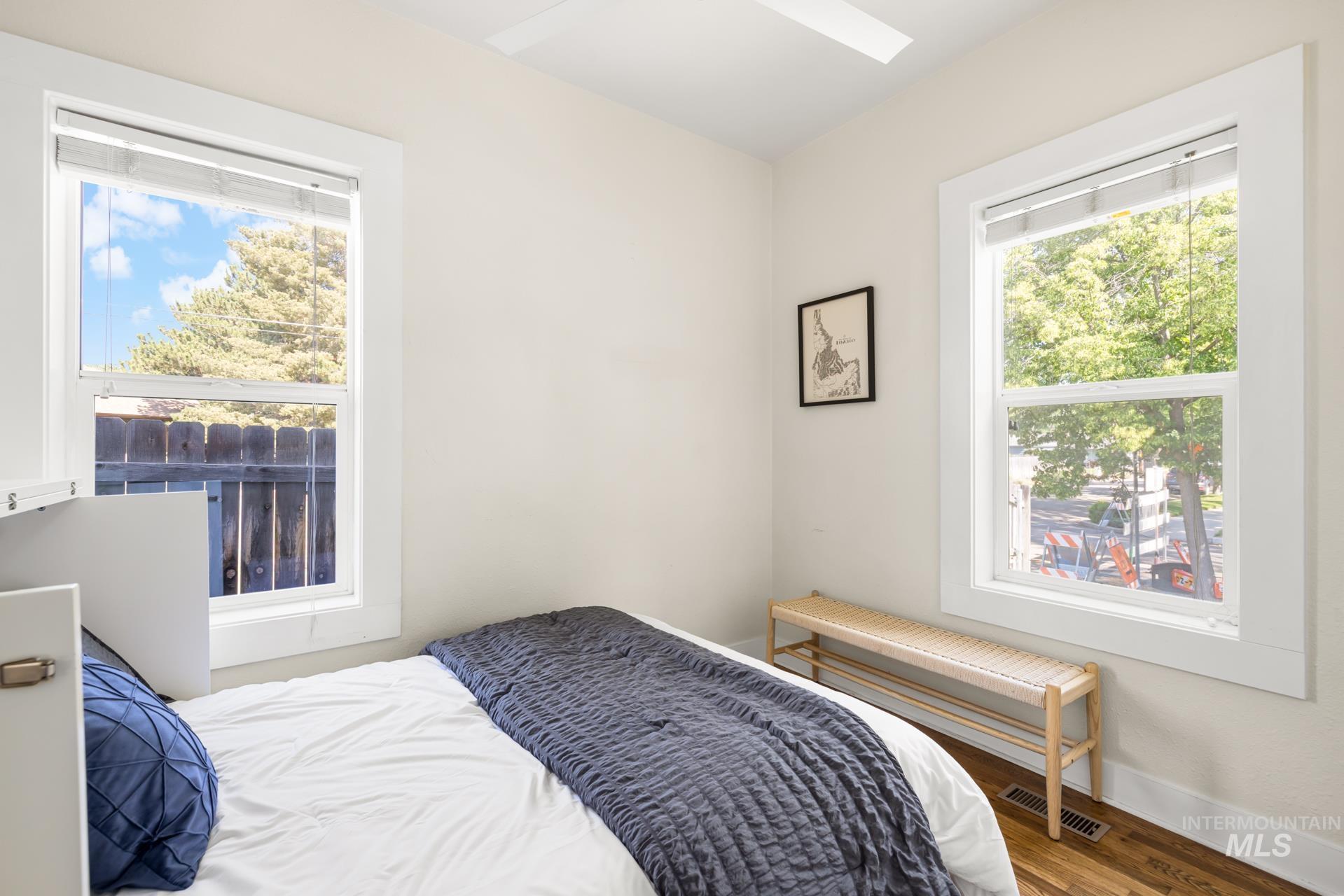 Bright room featuring two windows with white trim, a ceiling fan, light-toned wall paint, and wood-finish flooring