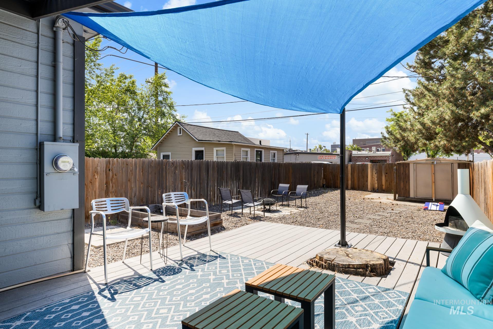 Outdoor entertaining area featuring a blue shade sail, wood-finish decking, gravel ground cover, and a full-height privacy fence