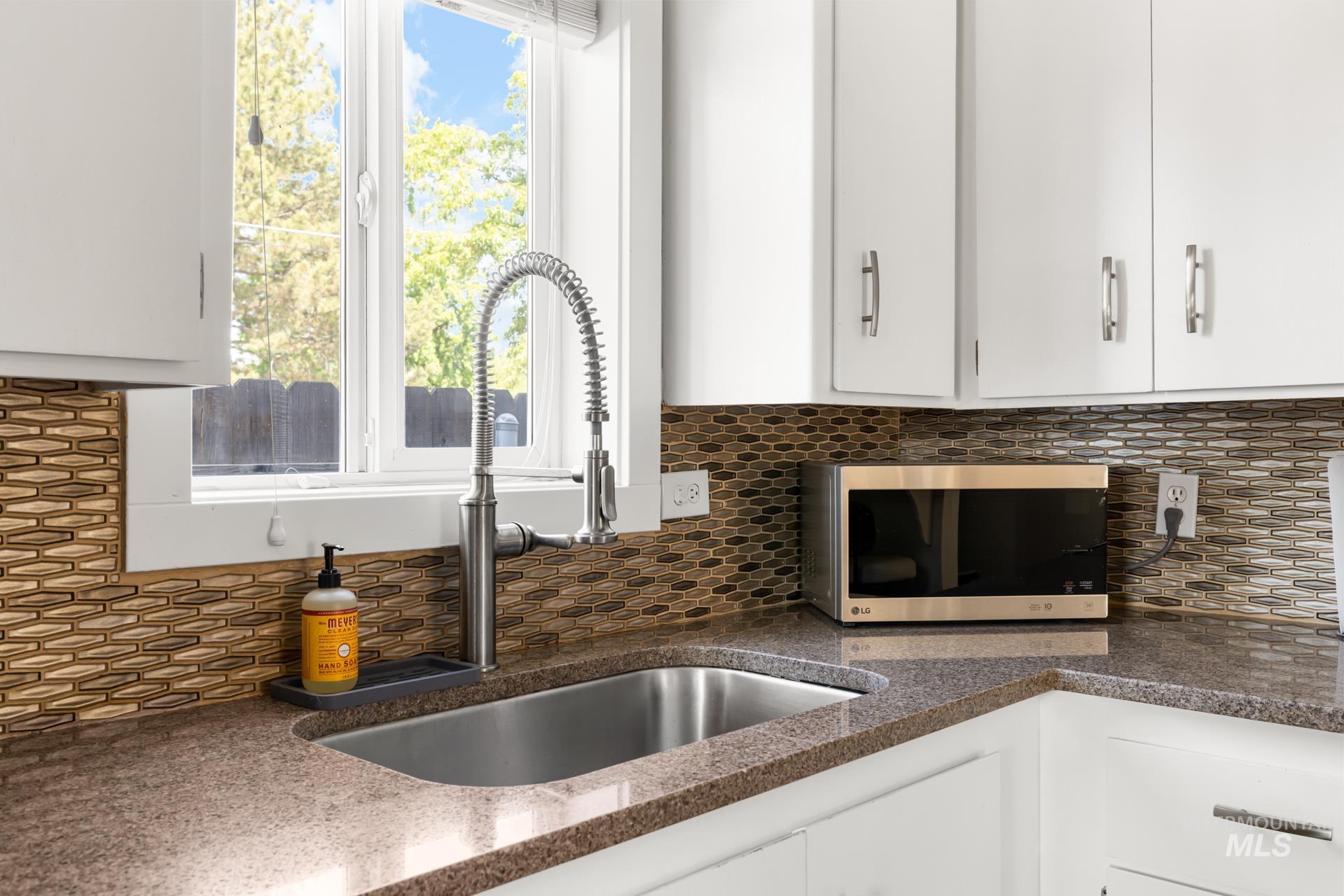 Kitchen featuring a stainless steel undermount sink with a coiled spring faucet, granite-look countertops, and a mosaic tile backsplash