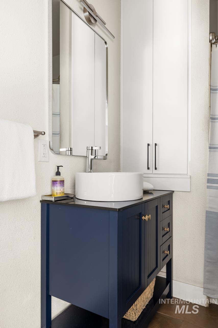 Bathroom featuring a navy blue vanity with gold-tone hardware, a white vessel sink, and a chrome faucet