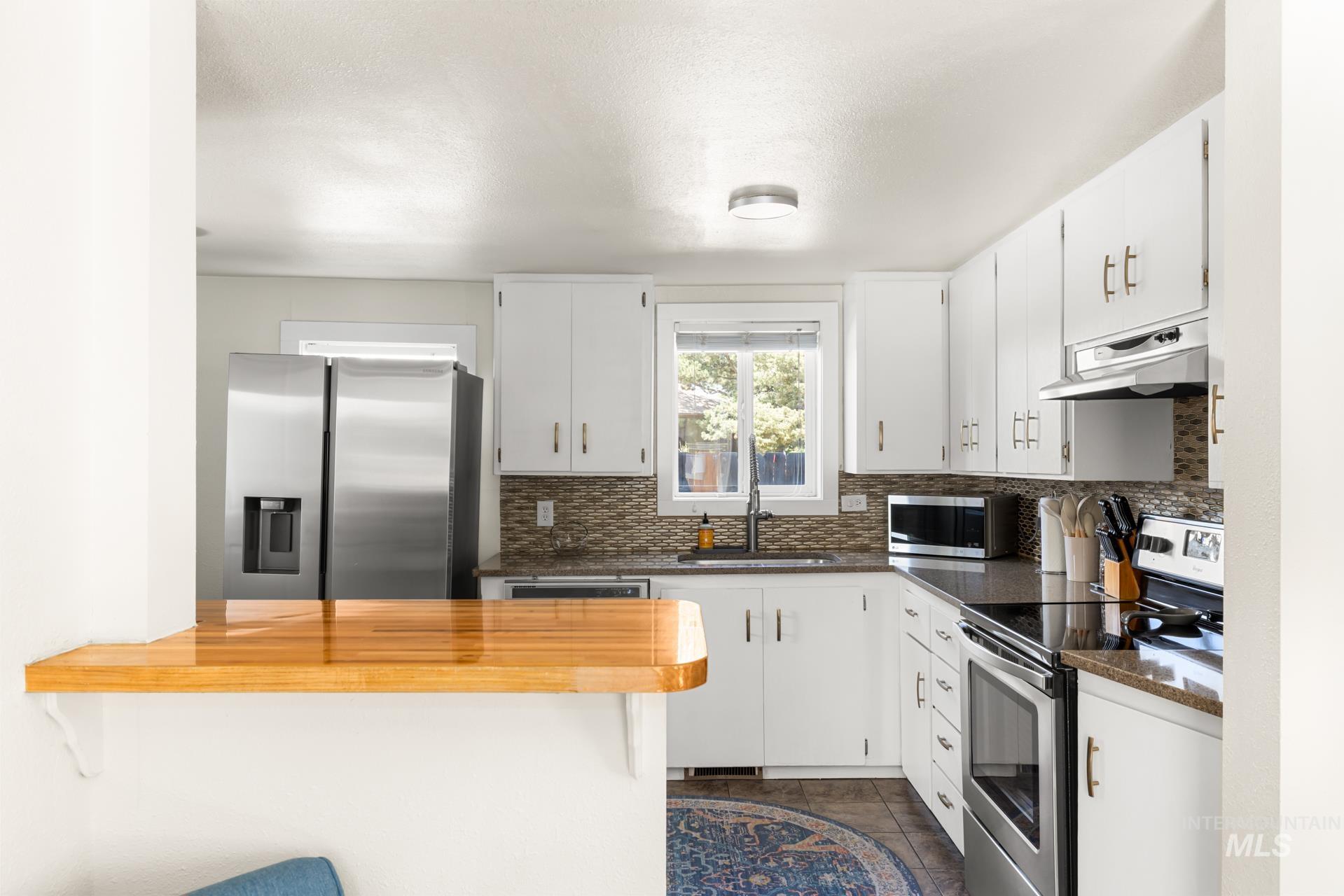 Kitchen featuring white cabinetry, stainless steel appliances, a mosaic tile backsplash, and dark countertops