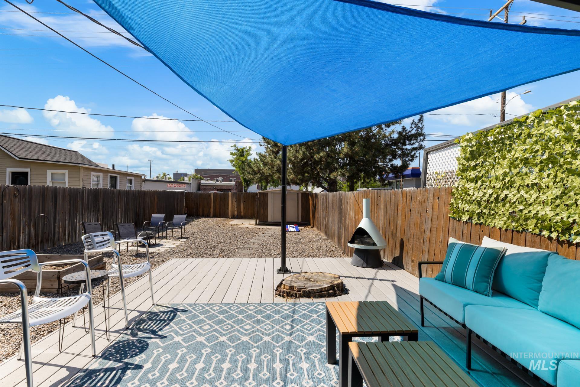 Outdoor patio featuring a blue shade sail, wood-finish decking, and a decorative privacy screen with green foliage