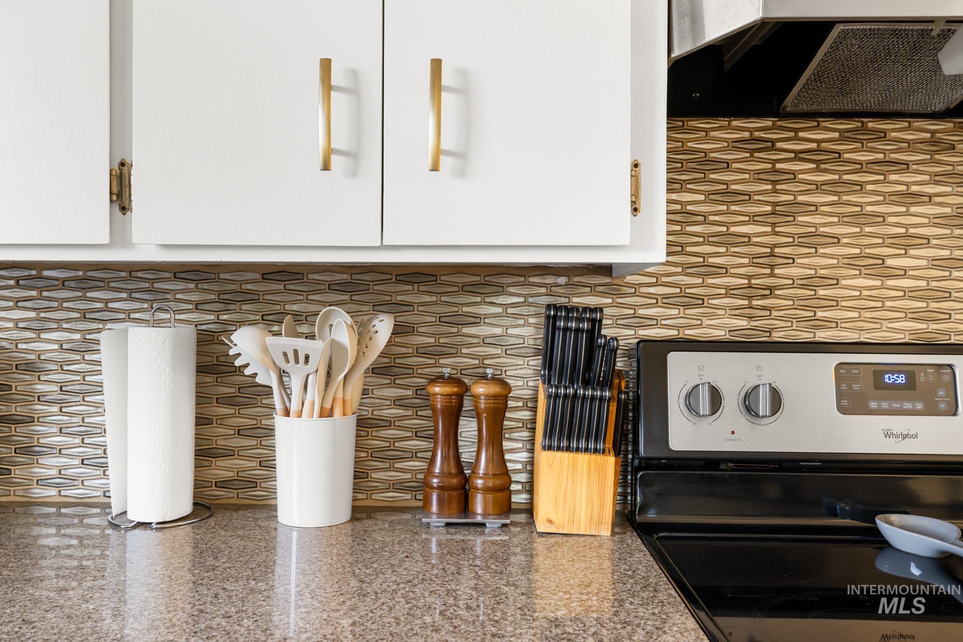 Kitchen featuring light-toned upper cabinetry with gold-tone hardware, a patterned tile backsplash, and a built-in range