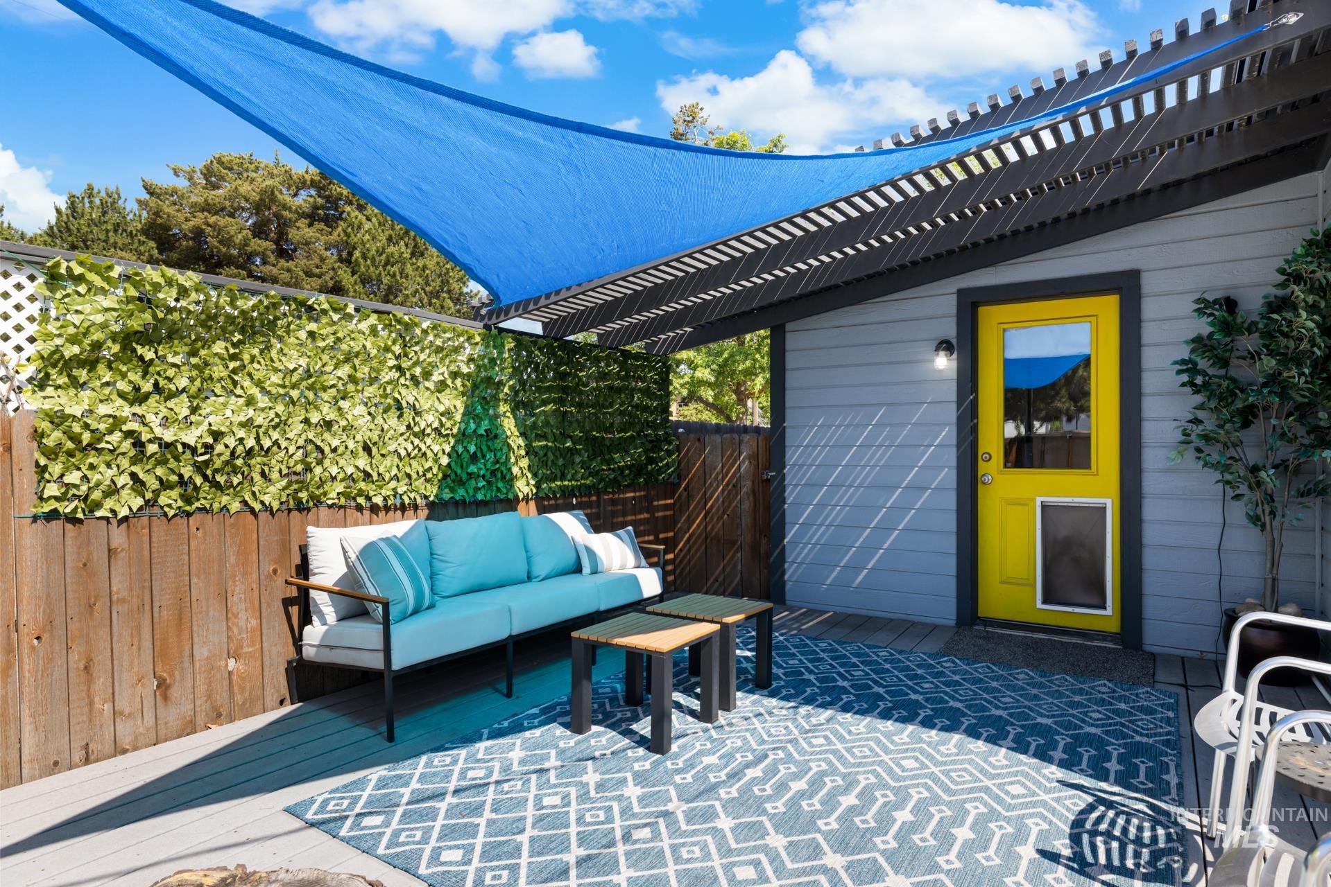 Outdoor patio featuring a blue shade sail, dark wood pergola, and light grey siding