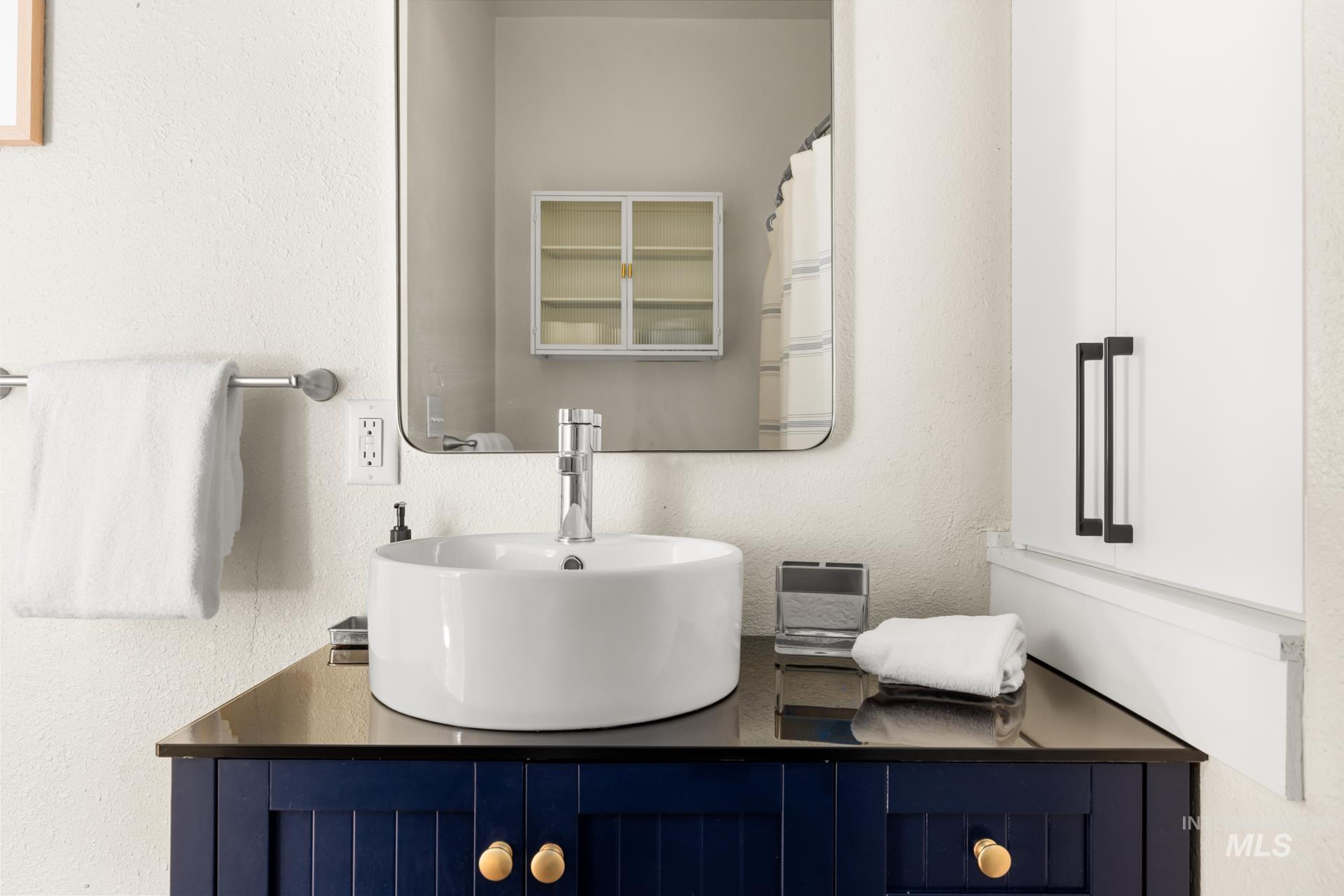 Modern vanity featuring a vessel sink with a chrome faucet, dark countertop, and blue cabinetry with gold-tone hardware