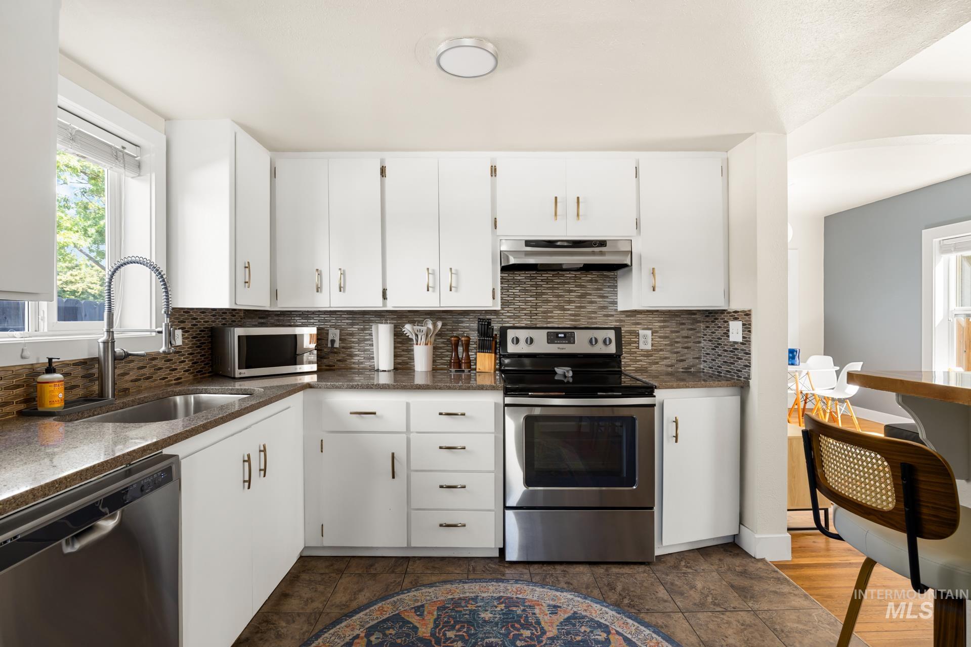 Kitchen featuring white cabinetry, a stainless steel electric range, a stainless steel dishwasher, a mosaic tile backsplash, and dark speckled countertops
