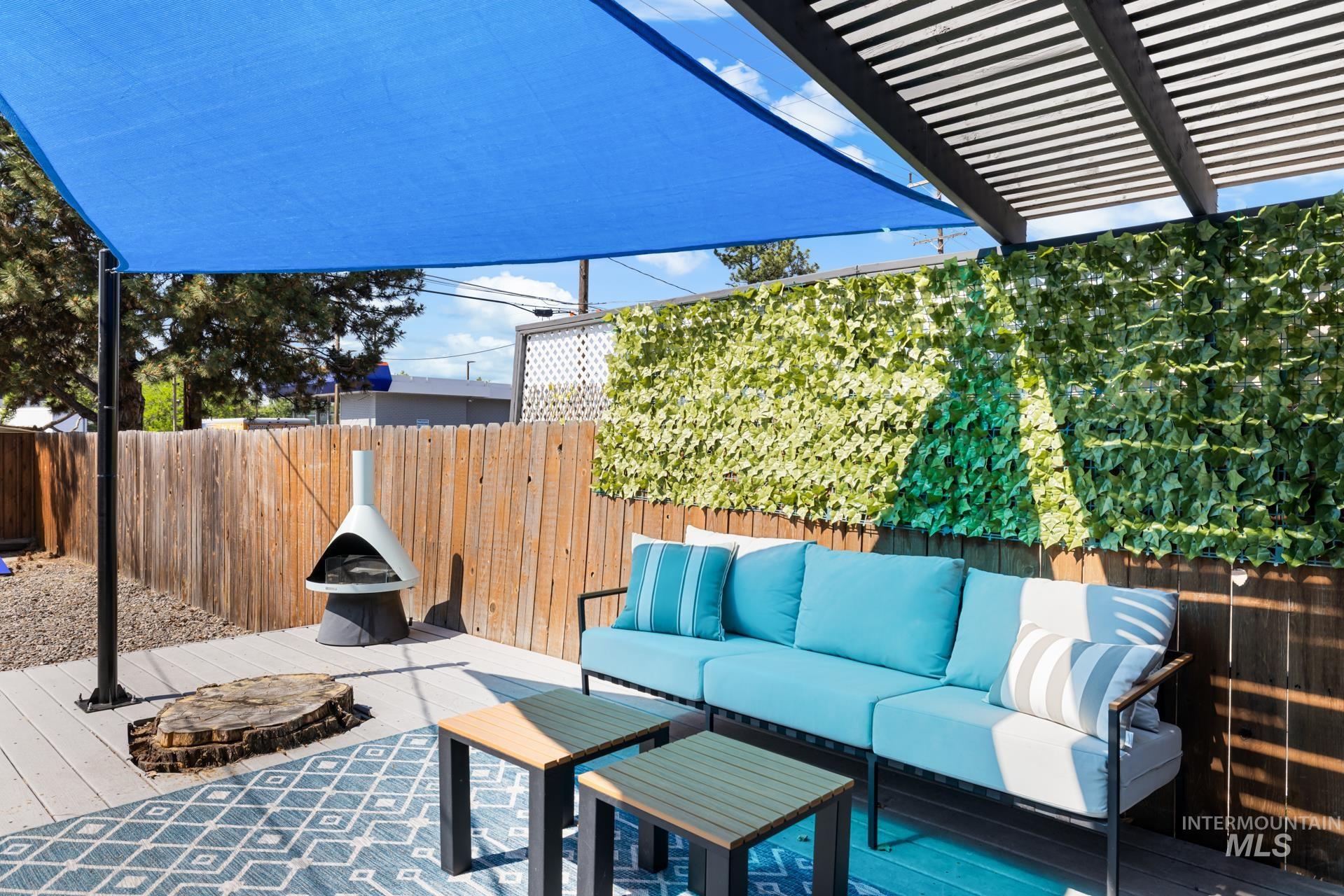 Expansive outdoor living area featuring a wood-finish deck, an overhead pergola, and a vibrant blue shade sail