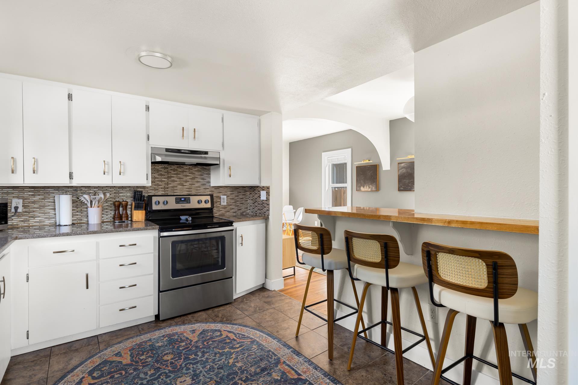 Kitchen featuring white cabinetry, a neutral mosaic tile backsplash, and a stainless steel electric range with an overhead microwave
