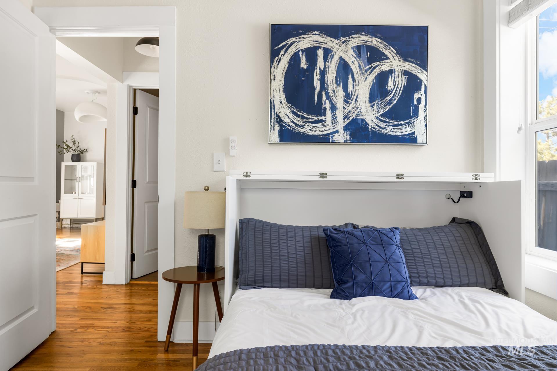 Built-in wall bed with integrated headboard and overhead storage, hardwood-finish flooring, white trim, and a window with natural light