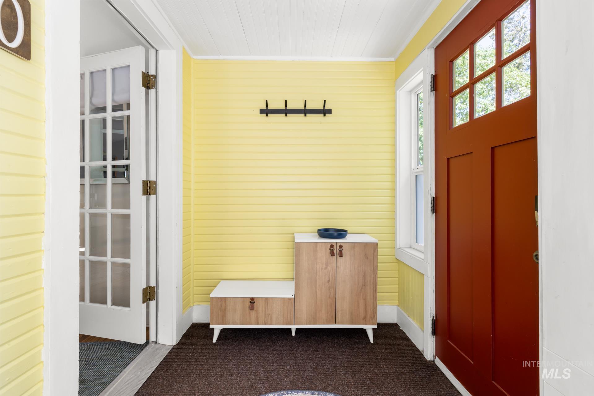 Entryway featuring a rich red paneled front door with upper lites, horizontal yellow wall paneling, white trim, and a white beadboard ceiling