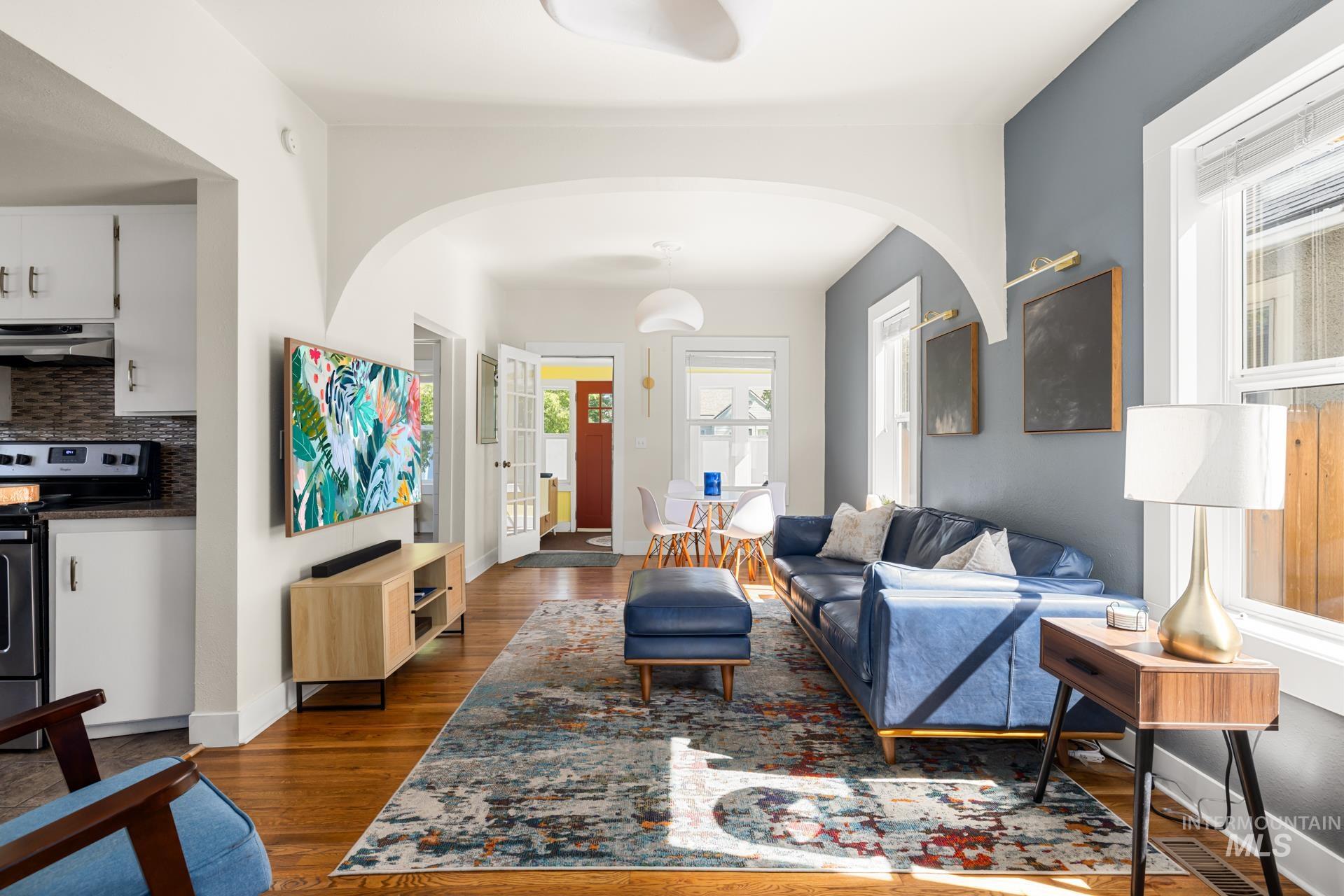 Living area featuring hardwood flooring, white painted walls, and an arched entryway
