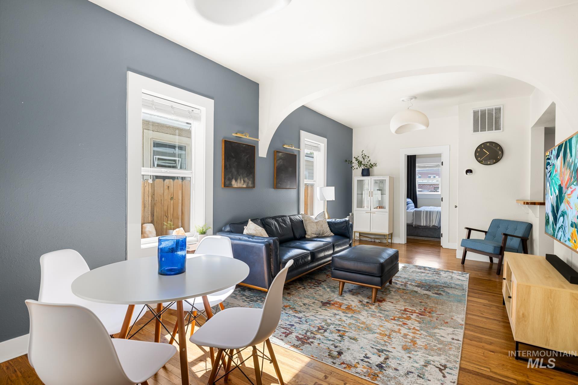 Living area with hardwood flooring, arched doorways, a dining space with a circular table, and windows providing natural illumination