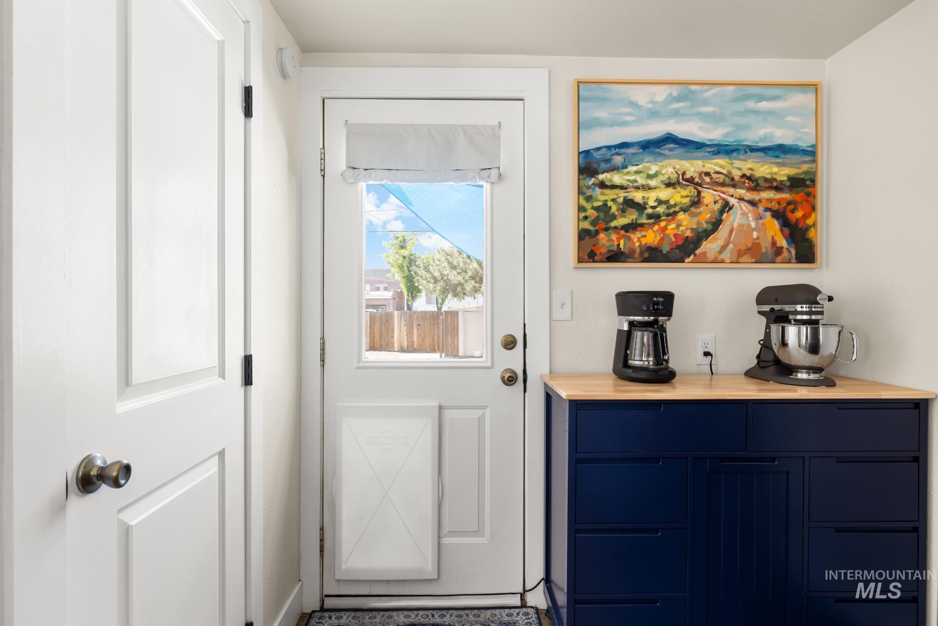 White paneled door with brass hardware, frosted glass exterior door with a roll-up shade, blue cabinetry with matte black hardware, and a wood-finish countertop