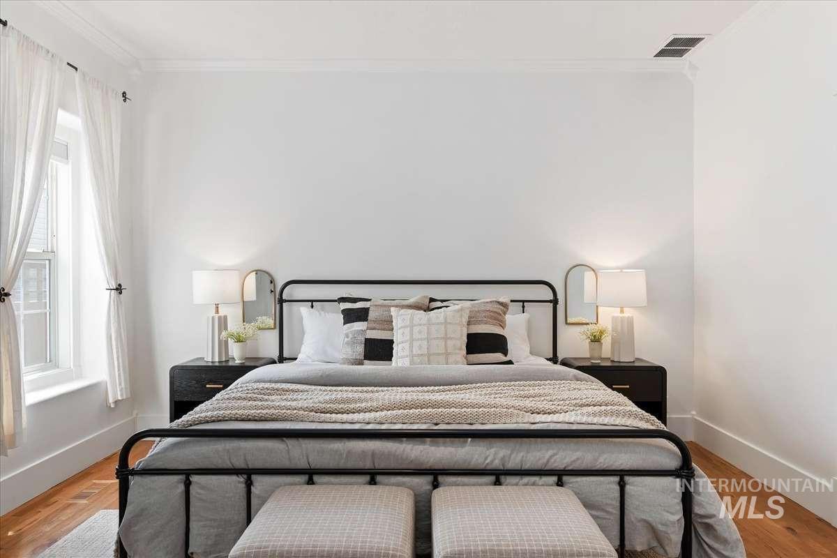 Light-filled bedroom featuring wood-finish flooring, white walls, crown molding, and a double-hung window