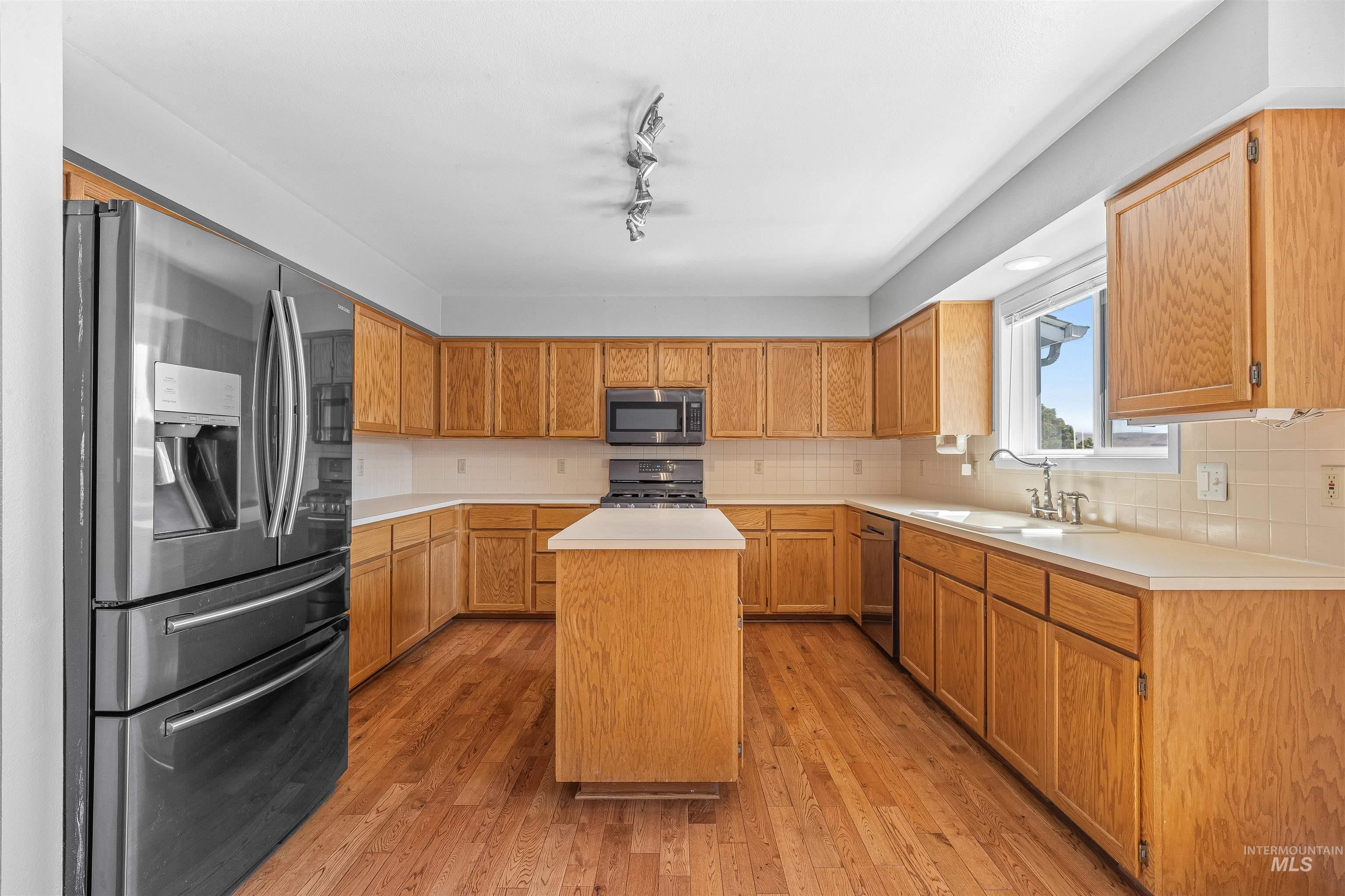Kitchen with appliances with stainless steel finishes, a center island, light wood finished floors, light countertops, and backsplash