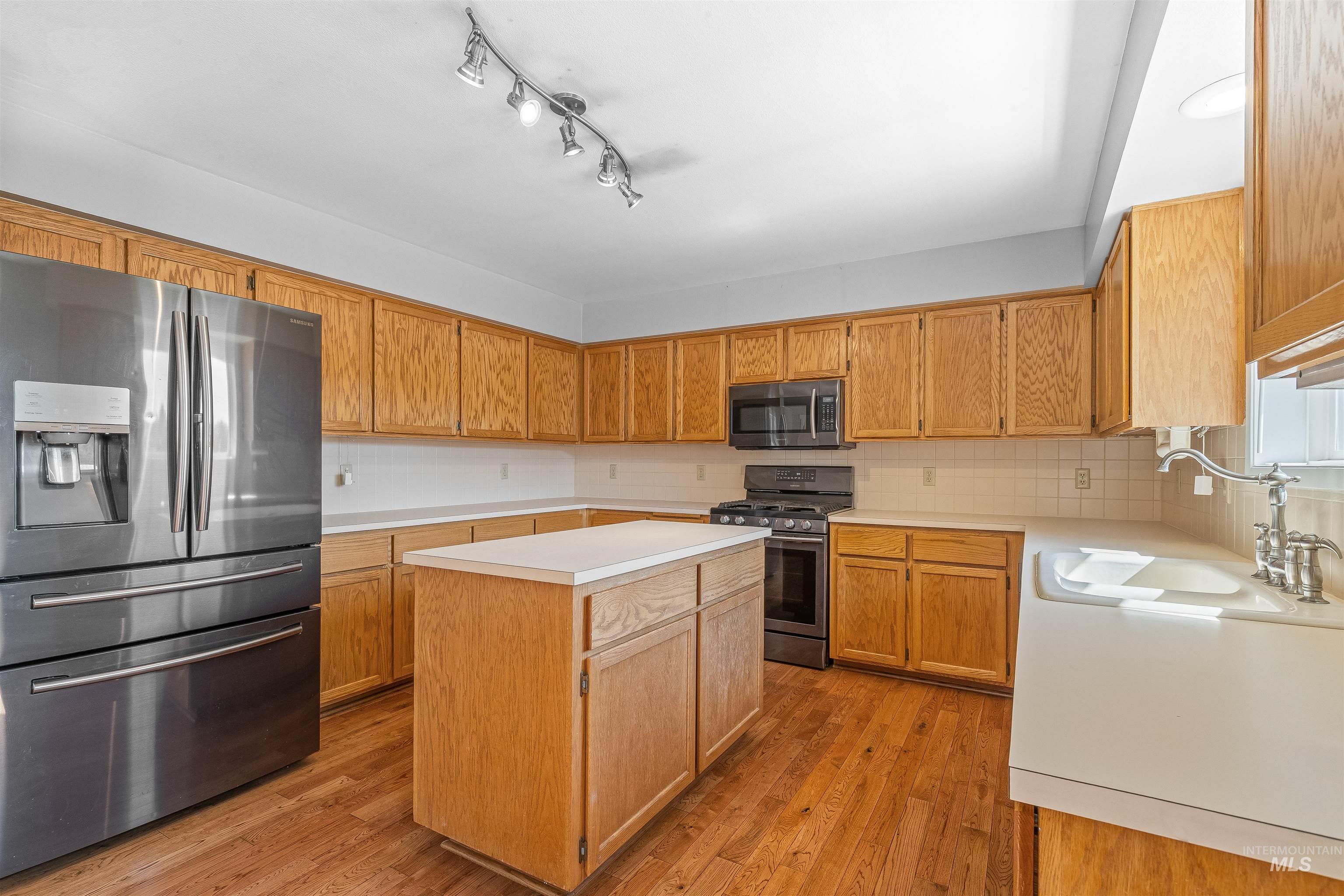 Kitchen featuring appliances with stainless steel finishes, light countertops, a kitchen island, light wood-style flooring, and tasteful backsplash