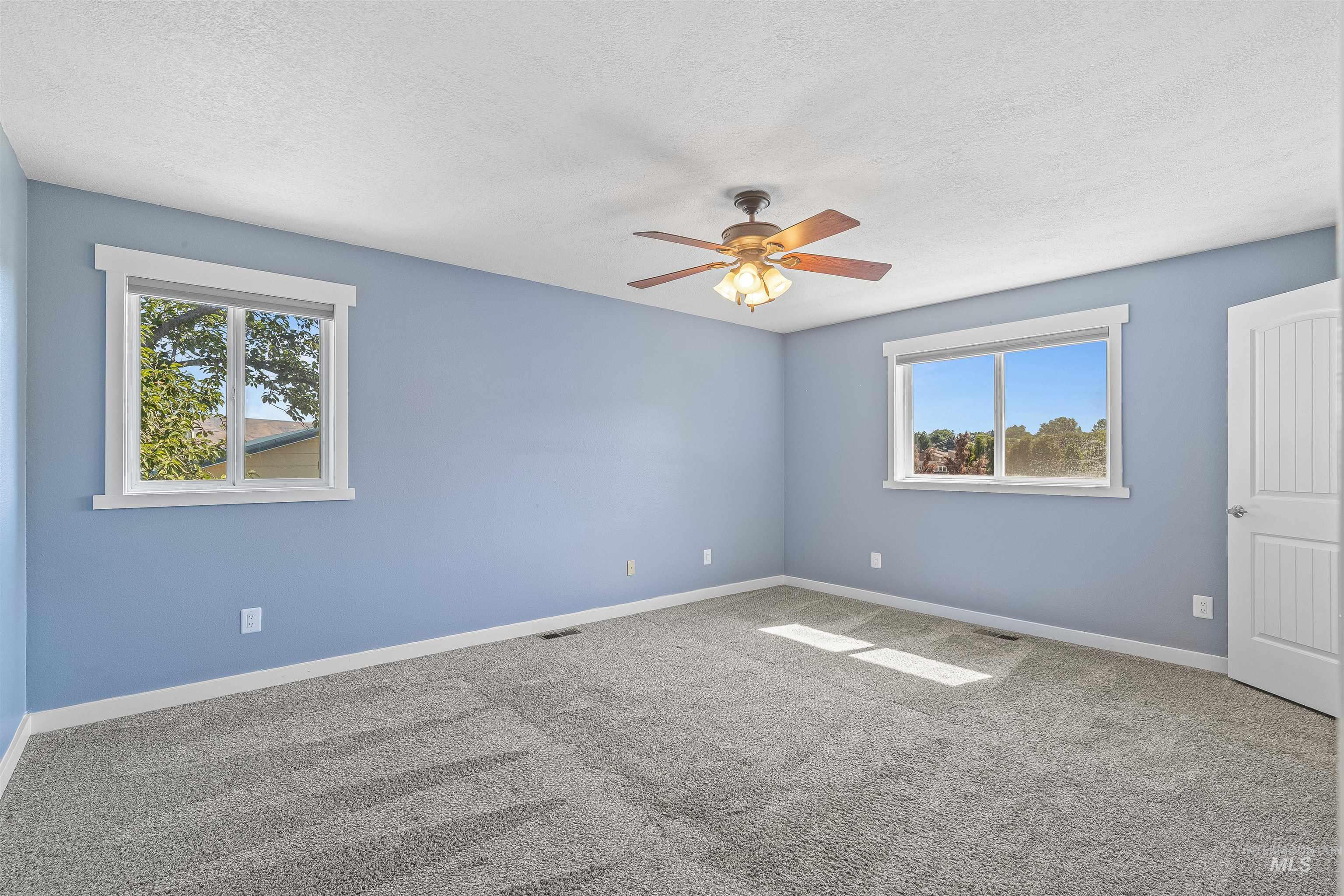 Carpeted spare room featuring plenty of natural light, a textured ceiling, and ceiling fan