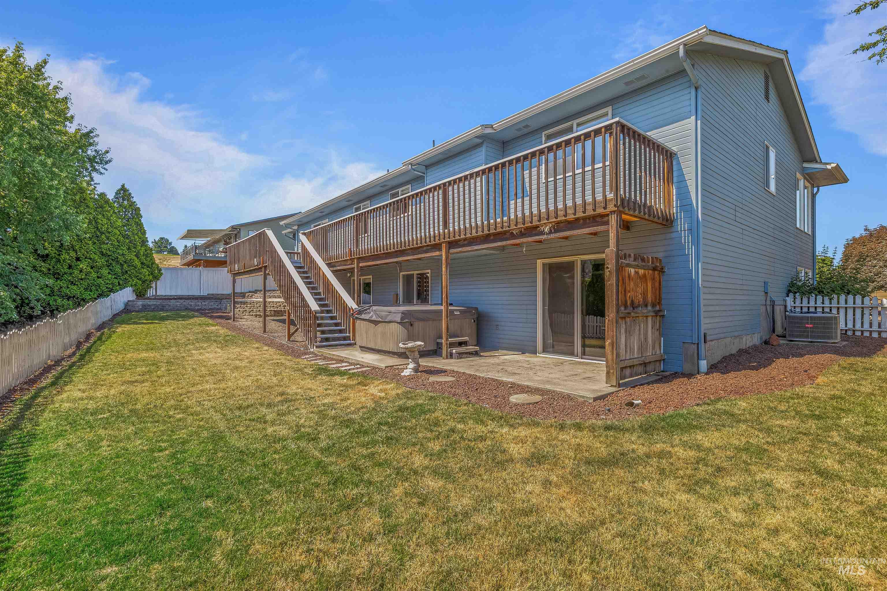 Rear view of house featuring a hot tub, a wooden deck, a fenced backyard, and a patio area