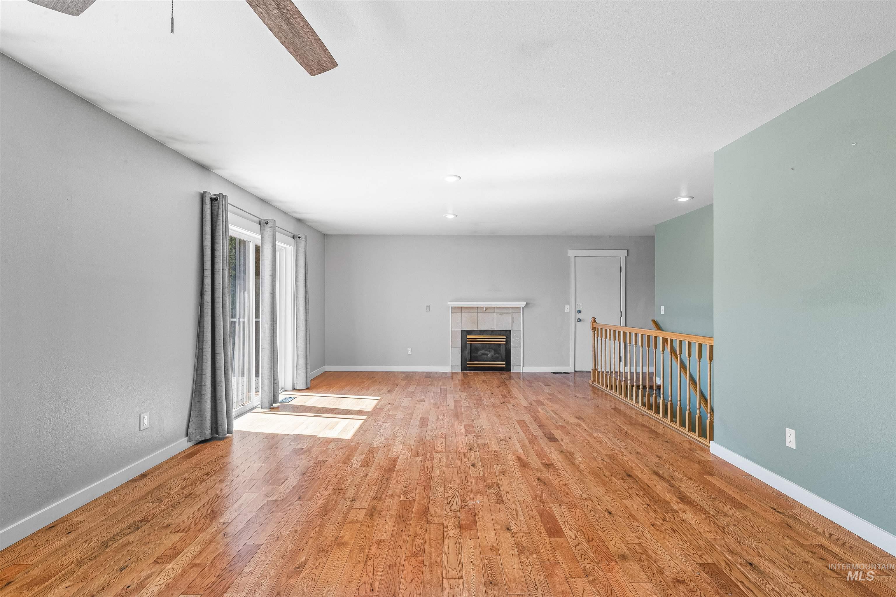 Unfurnished living room featuring light wood-style floors, a ceiling fan, and a tile fireplace