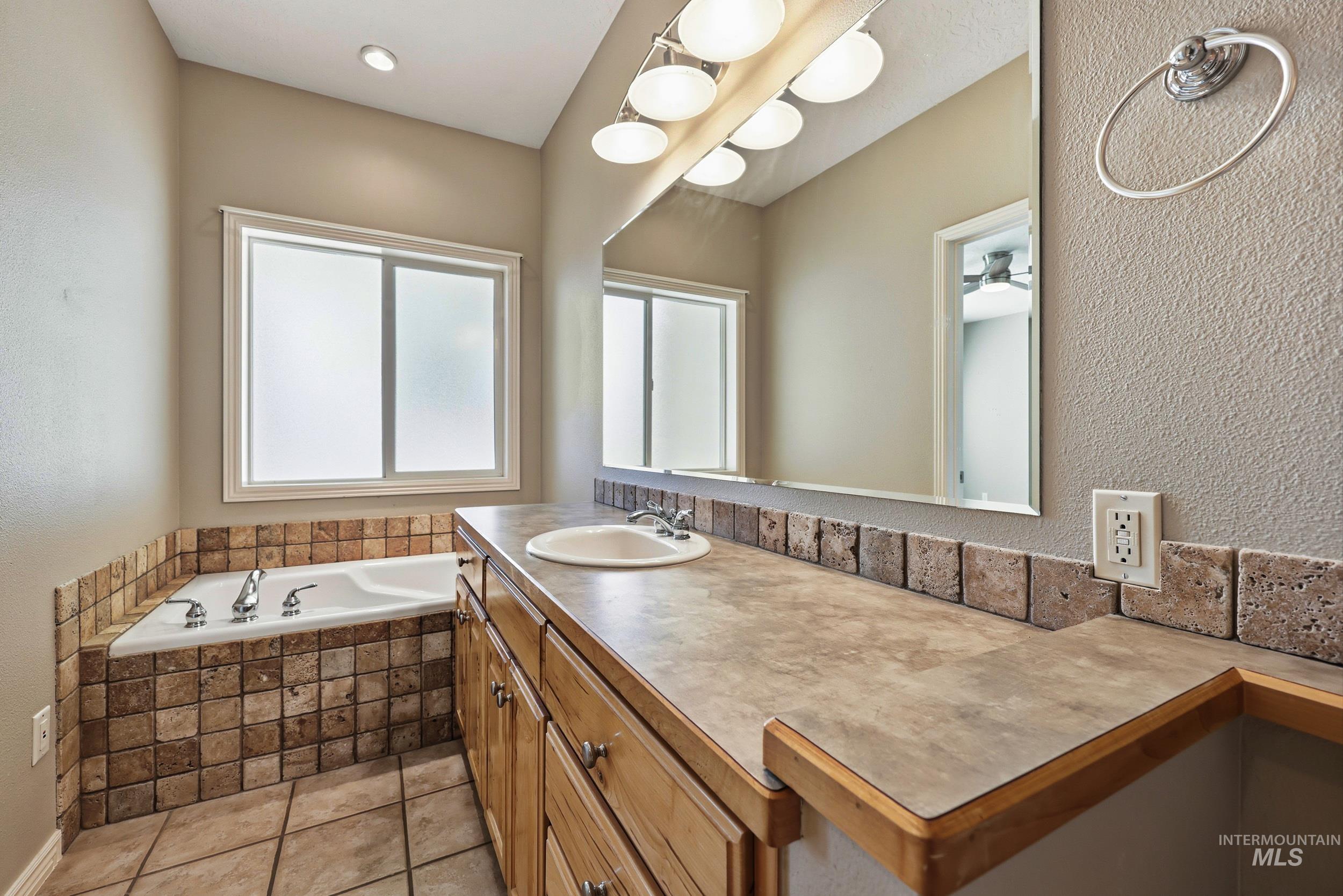 Bathroom featuring a textured wall, a bath, vanity, and light tile patterned flooring