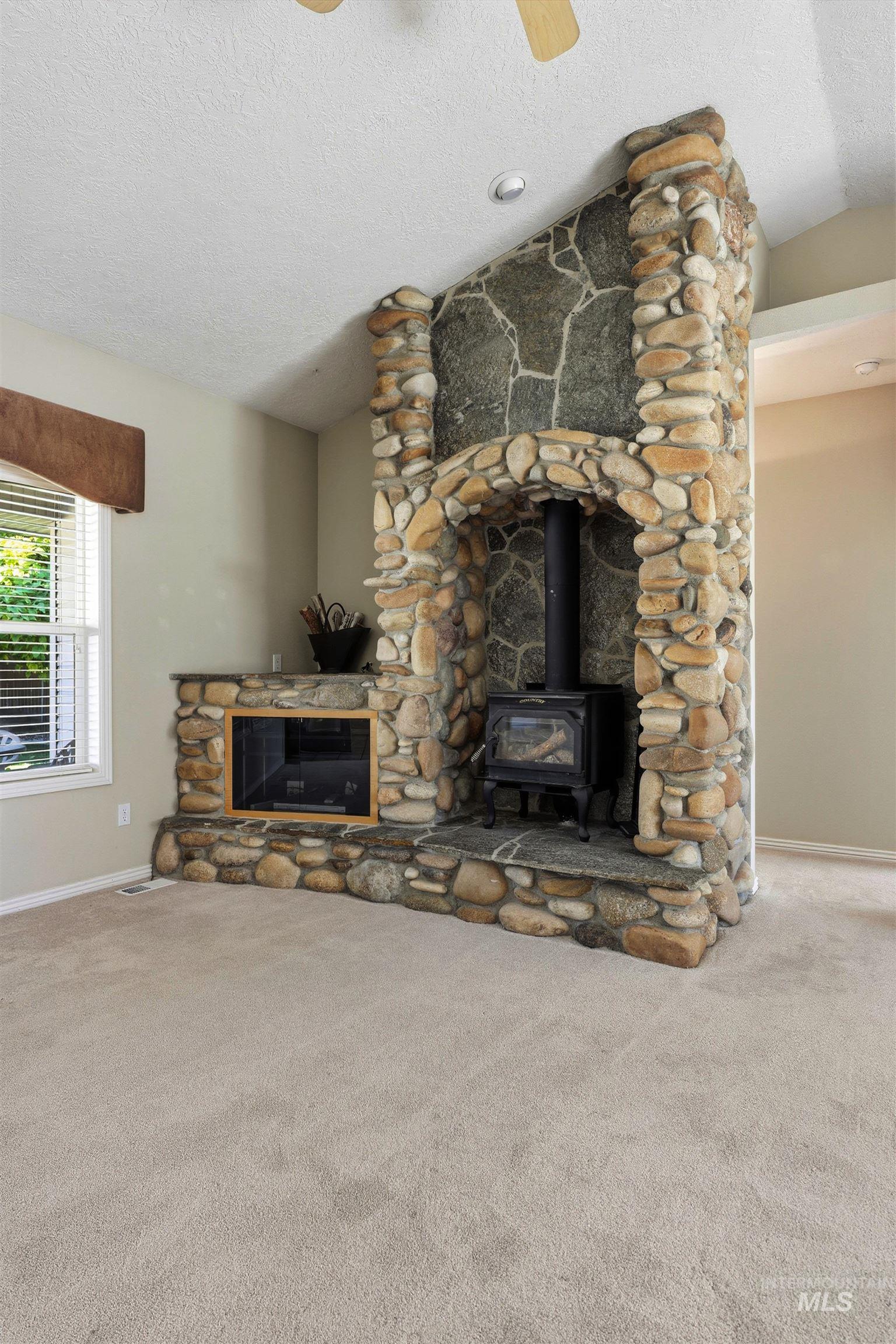 Unfurnished living room featuring a textured ceiling, a wood stove, carpet flooring, and lofted ceiling