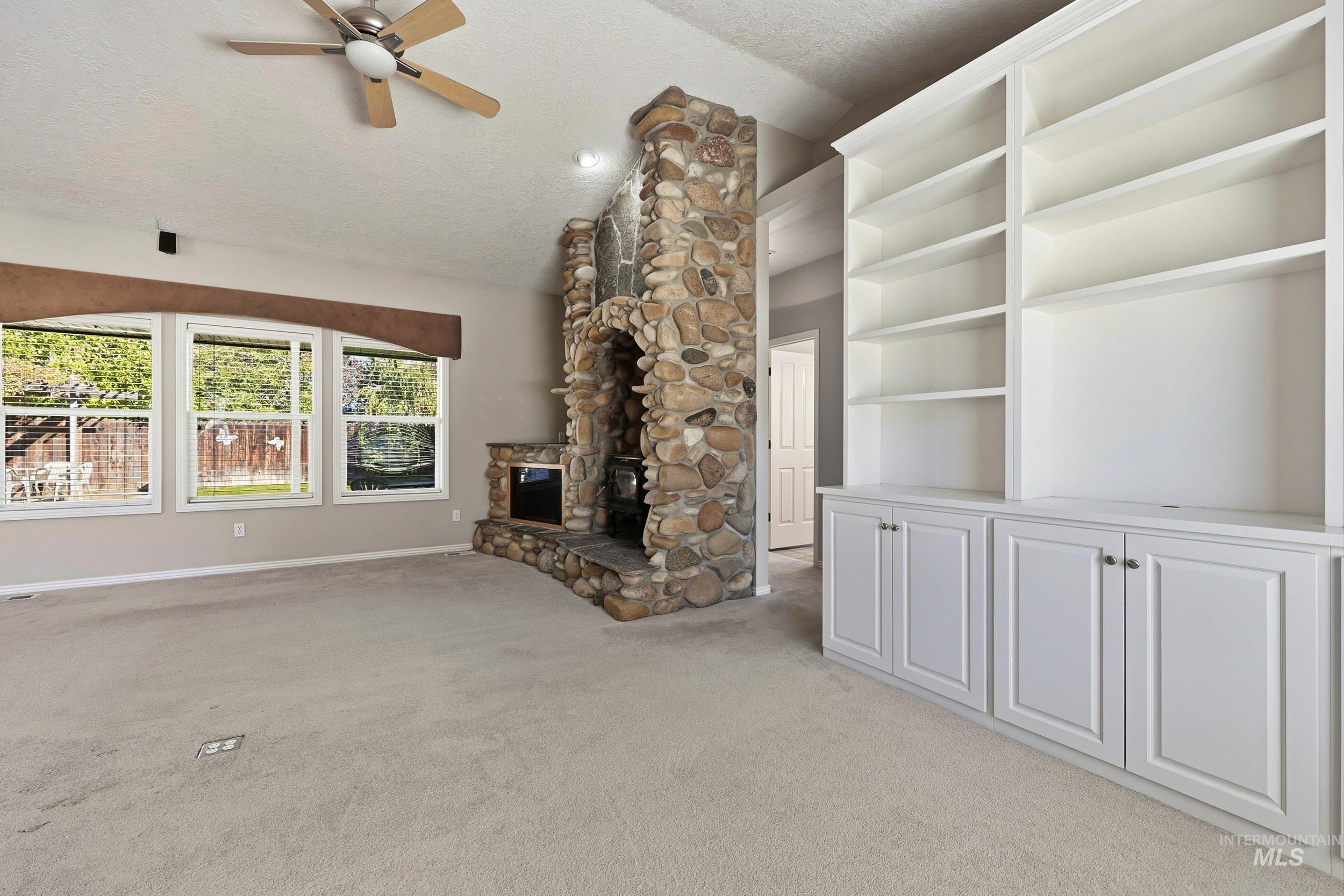 Unfurnished living room with a textured ceiling, vaulted ceiling, light colored carpet, a ceiling fan, and a fireplace