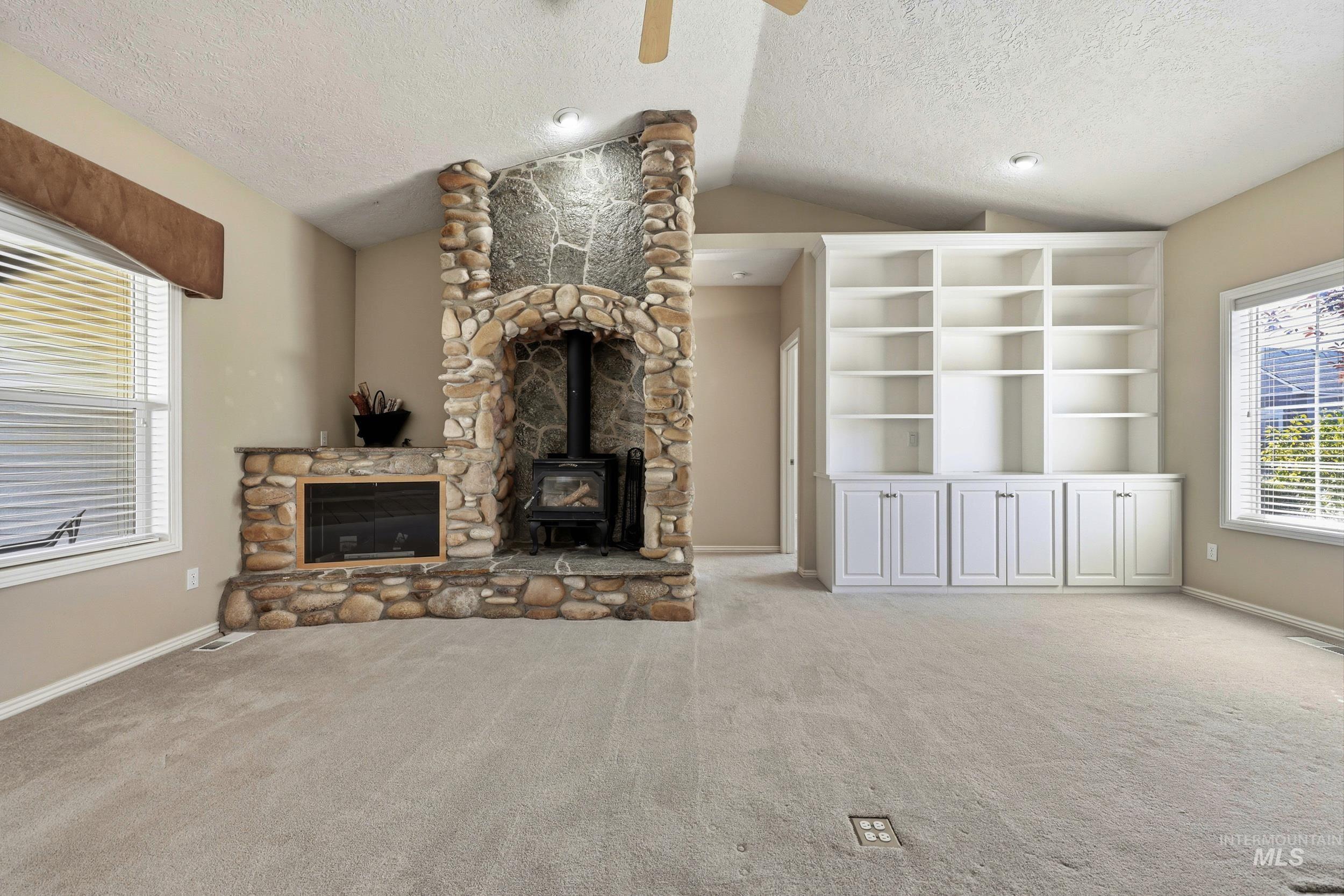 Unfurnished living room featuring a wood stove, lofted ceiling, light colored carpet, a textured ceiling, and ceiling fan