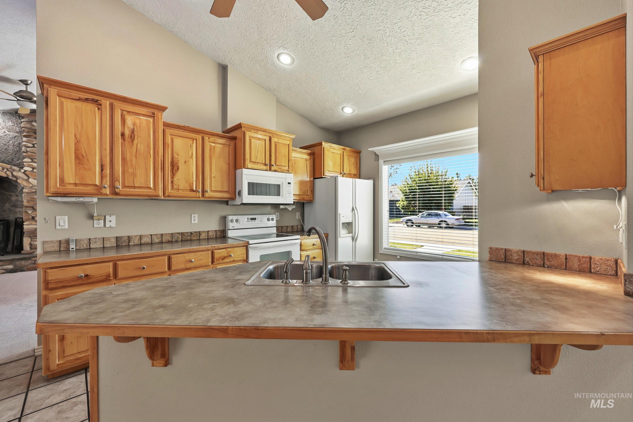 Kitchen with a breakfast bar area, ceiling fan, a textured ceiling, vaulted ceiling, and a peninsula