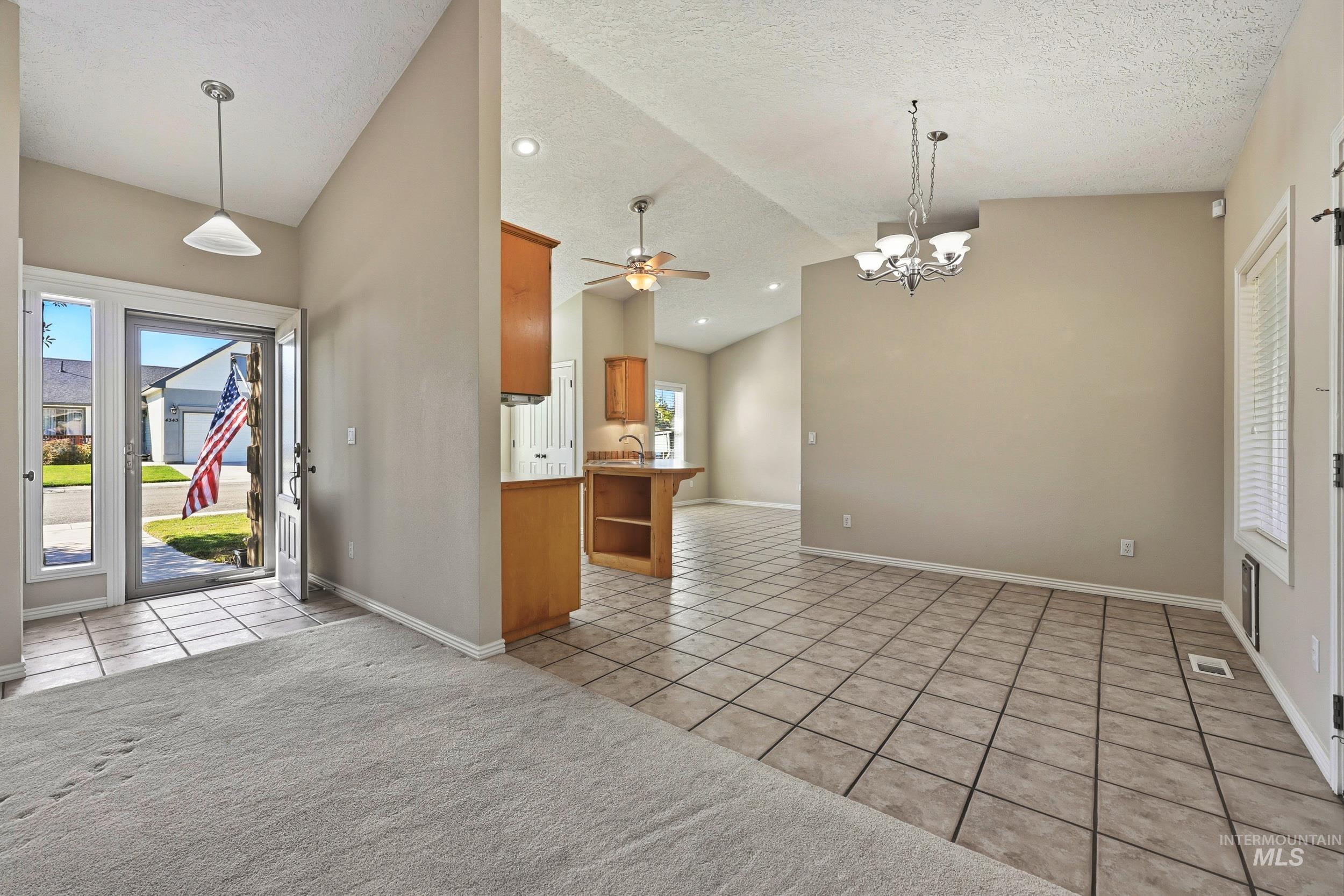Kitchen featuring light tile patterned flooring, brown cabinets, a chandelier, hanging light fixtures, and a textured ceiling